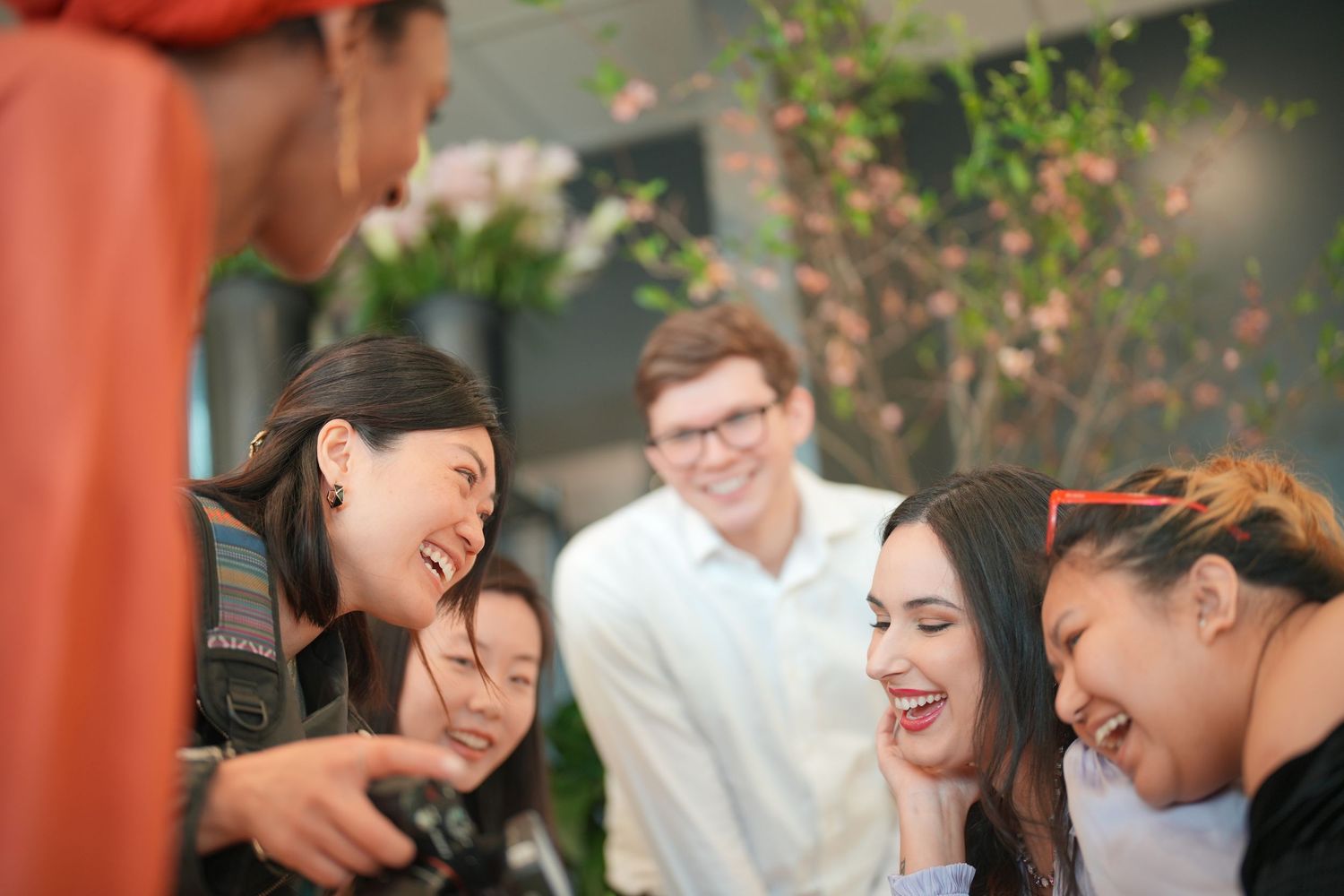 A diverse group of friends laughs together during a casual social gathering outdoors.