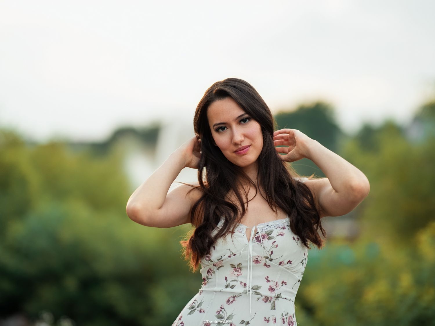 A woman in a floral dress poses outdoors during a sunny summer photoshoot in nature.