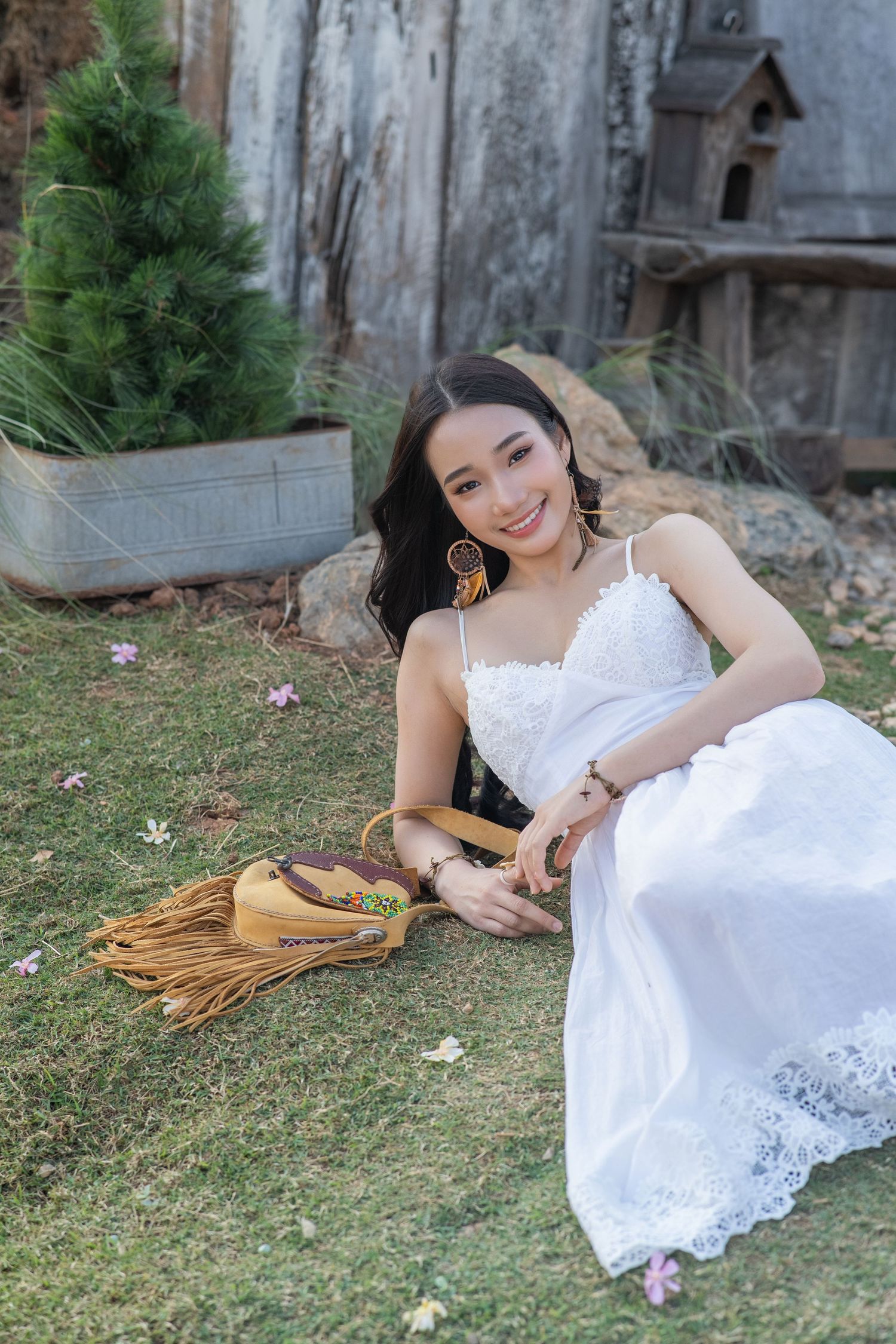 A woman in a white lace dress sits on grass beside a baseball glove in an outdoor garden setting.