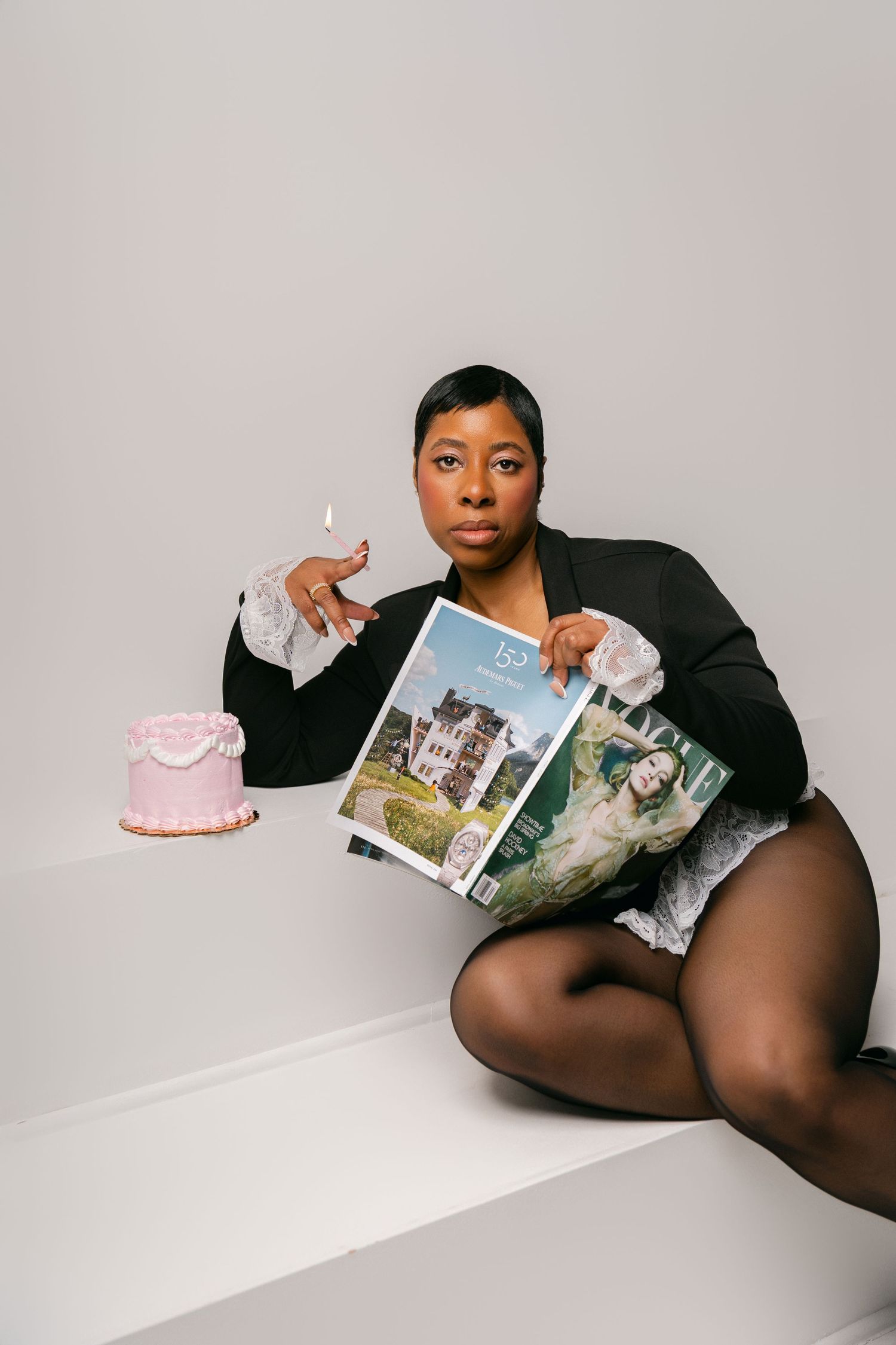 A photograph with a small pink cake and person holding photographic prints while sitting on a white surface.