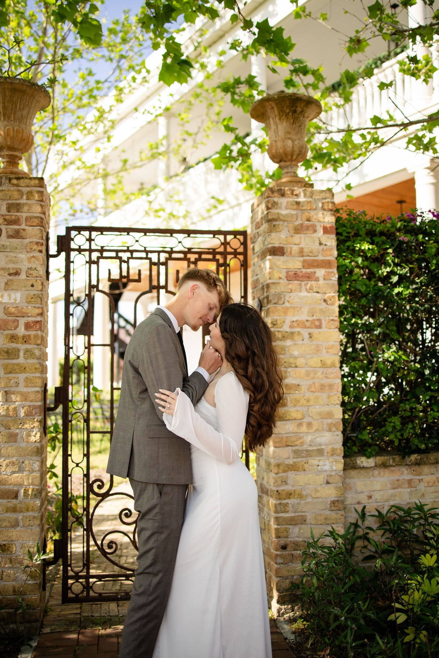 Romantic moment captured under a vine-covered pergola with brick columns and wrought iron details.