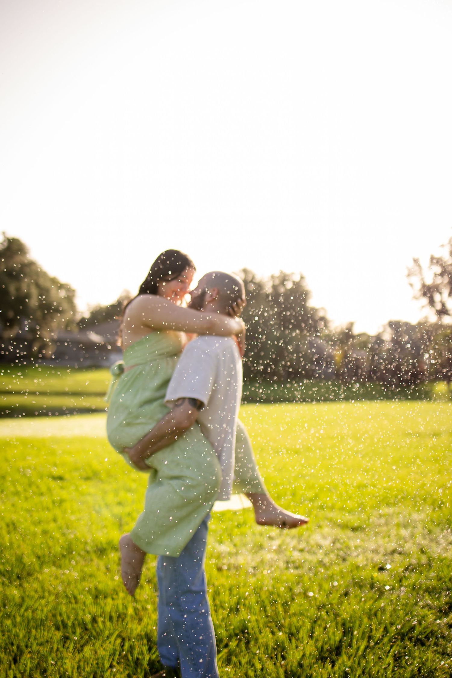 A romantic moment captured in a grassy field at sunset with water droplets sparkling in the golden light.