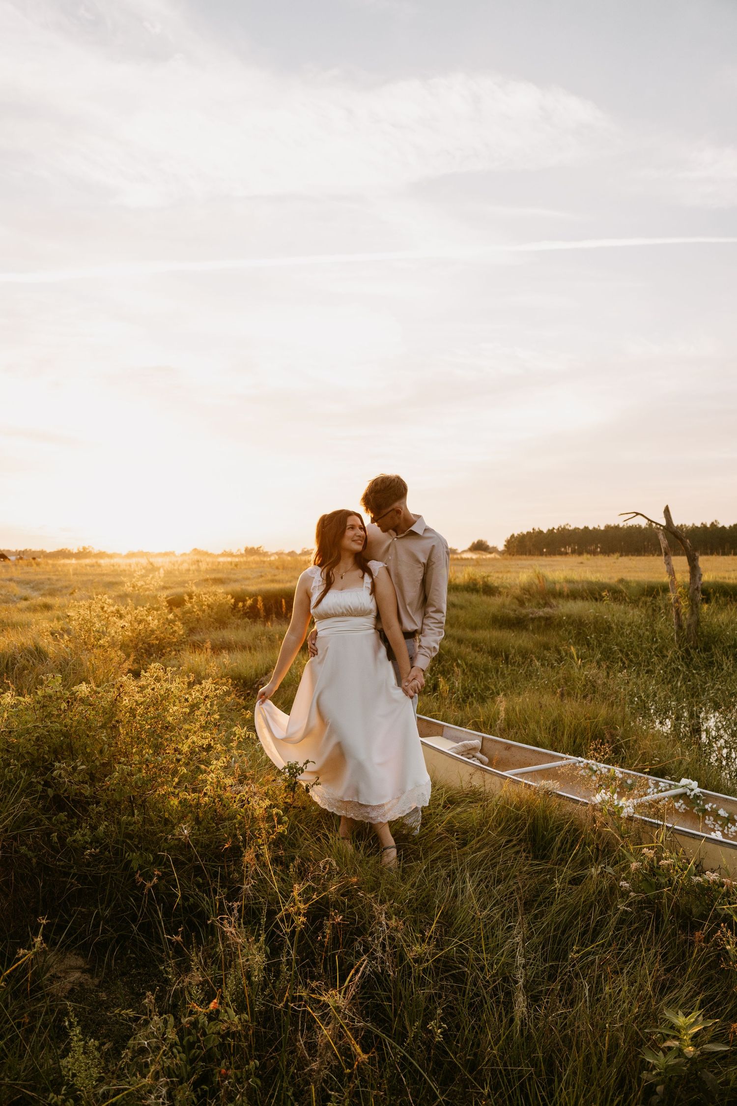 A couple walks through a serene meadow with tall grass during golden hour at sunset.