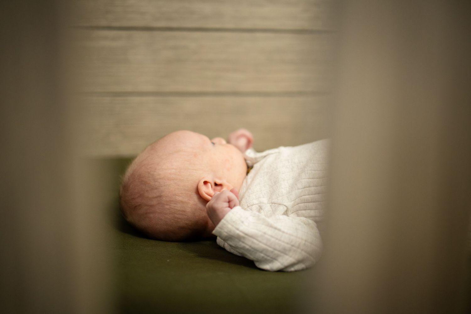 A sleeping baby swaddled in white fabric lies curled on a neutral background, captured in a gentle dreamy light.