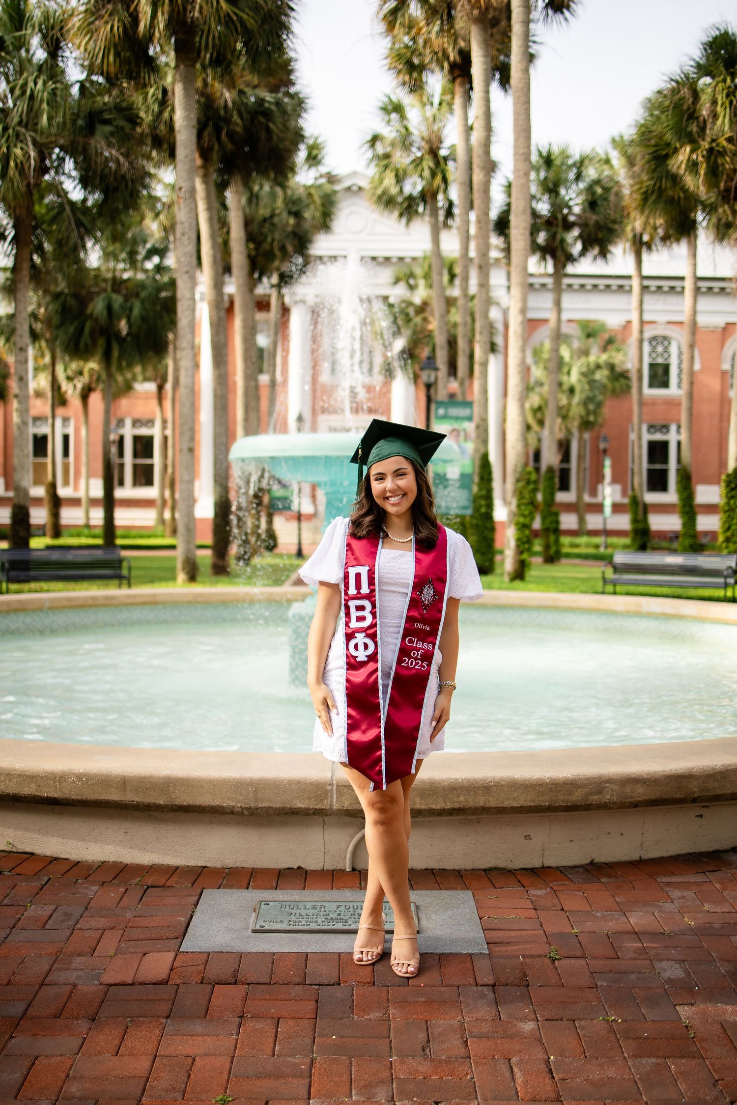 Graduation portraits taken by a fountain with palm trees and brick pavement at a university campus.