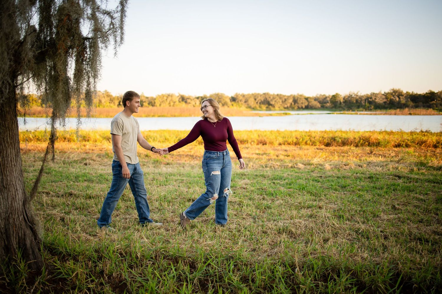 Two people playfully dance together in a golden field during sunset.