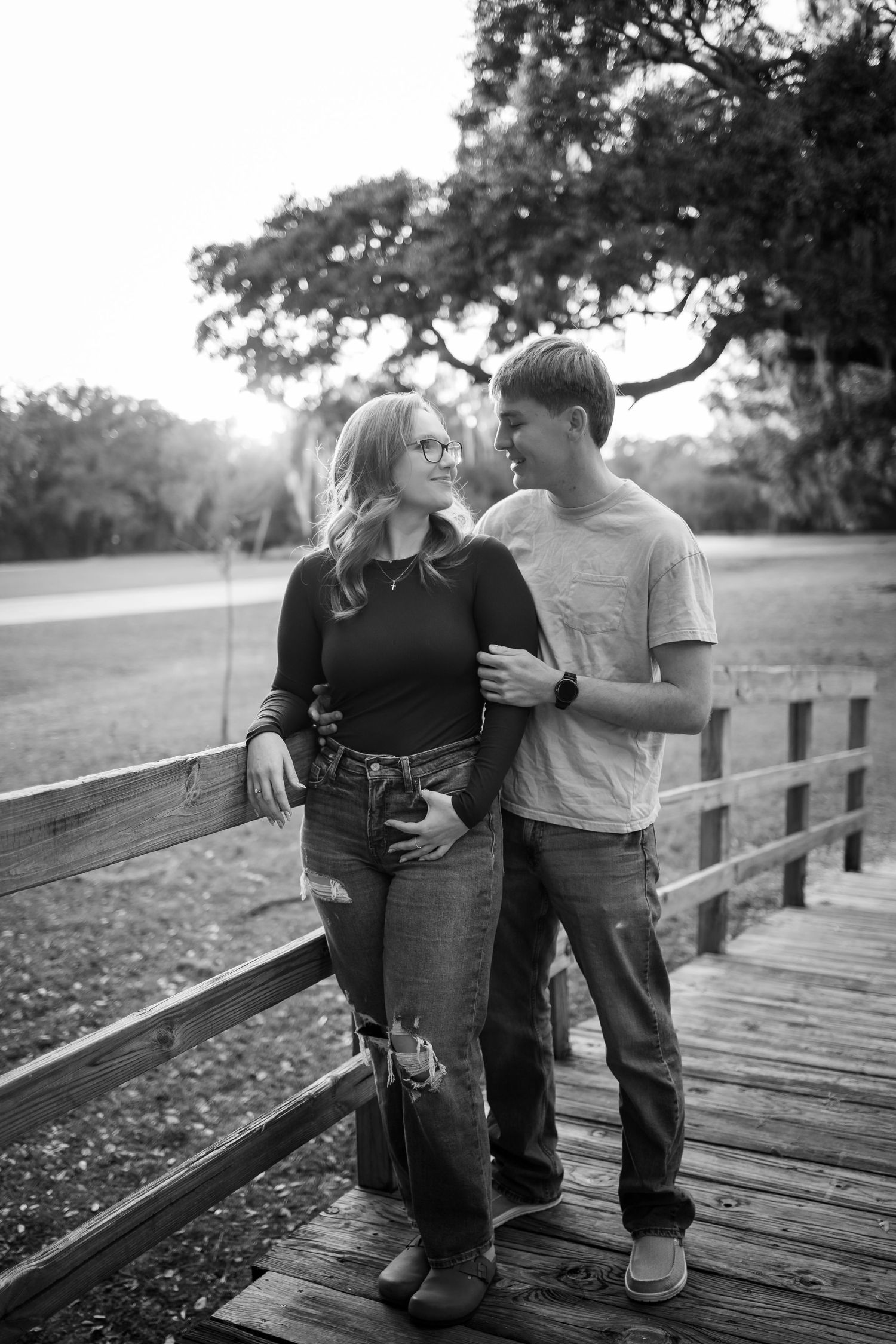 A romantic black and white portrait of a couple sharing an intimate moment on a wooden bridge.