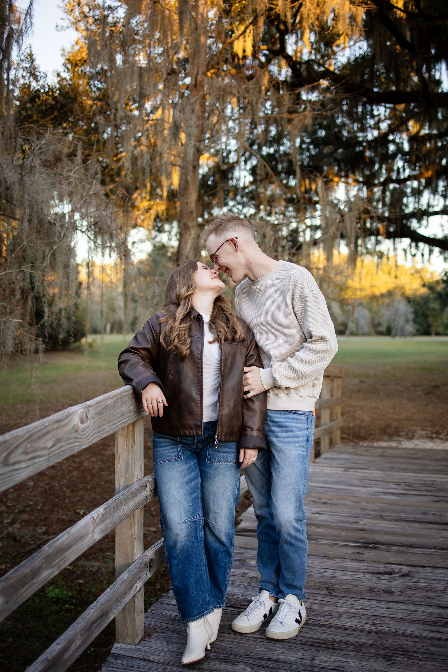 Couple sharing an intimate moment on wooden boardwalk under Spanish moss at sunset.
