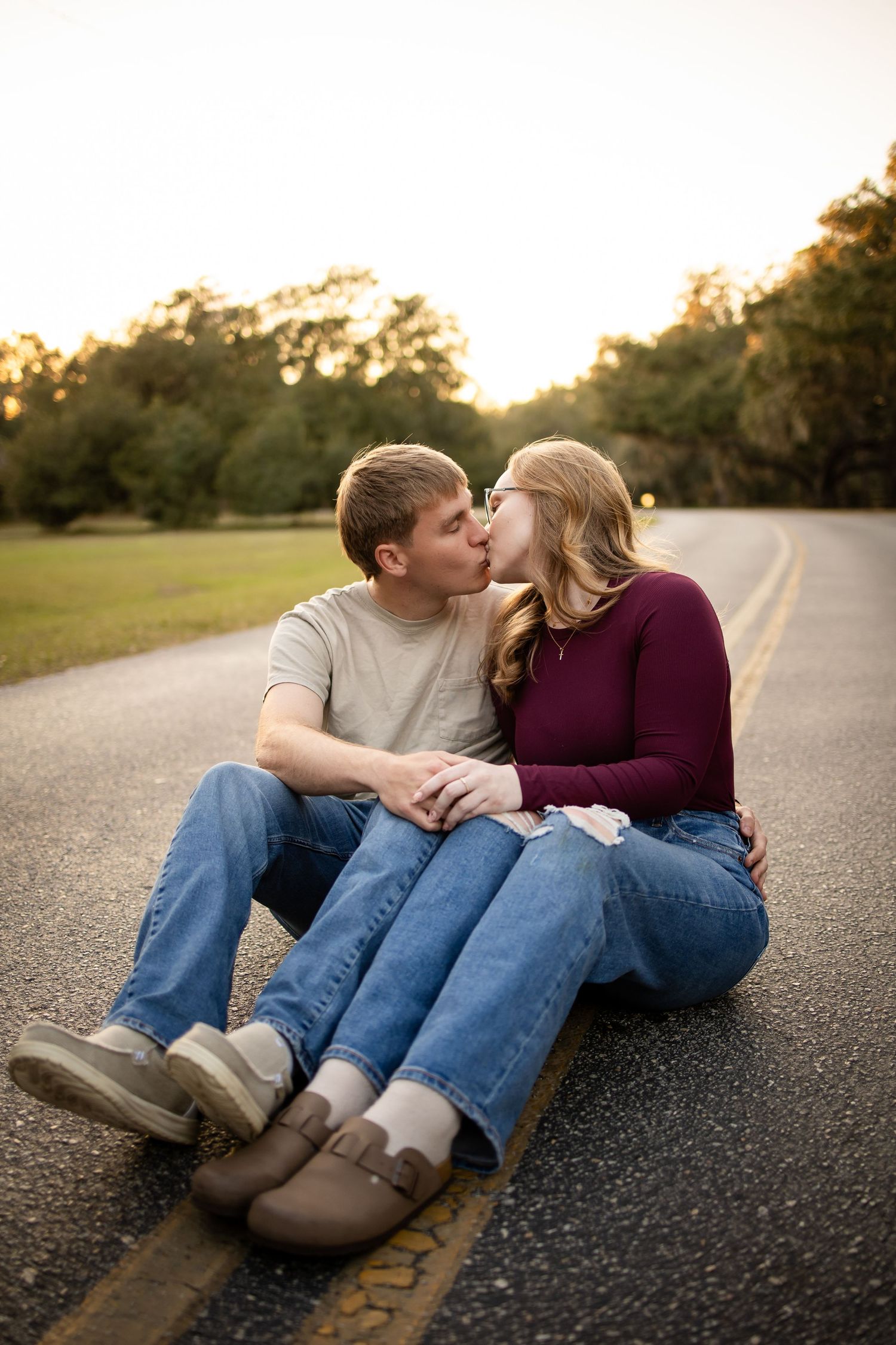 A couple sits close together on asphalt during a warm sunset photoshoot.