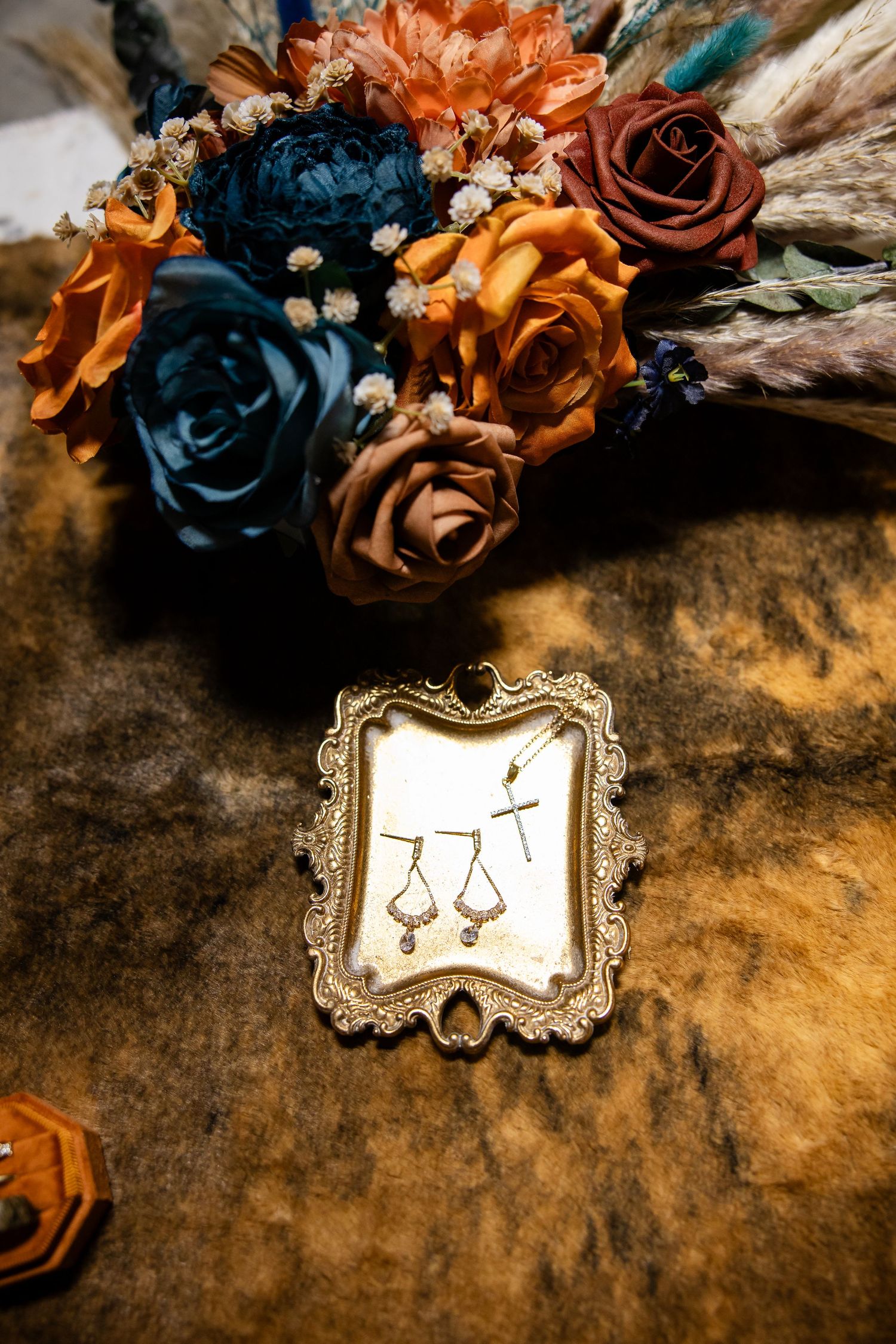 Boho wedding jewelry display with cross and teardrop earrings beside colorful floral bouquet.