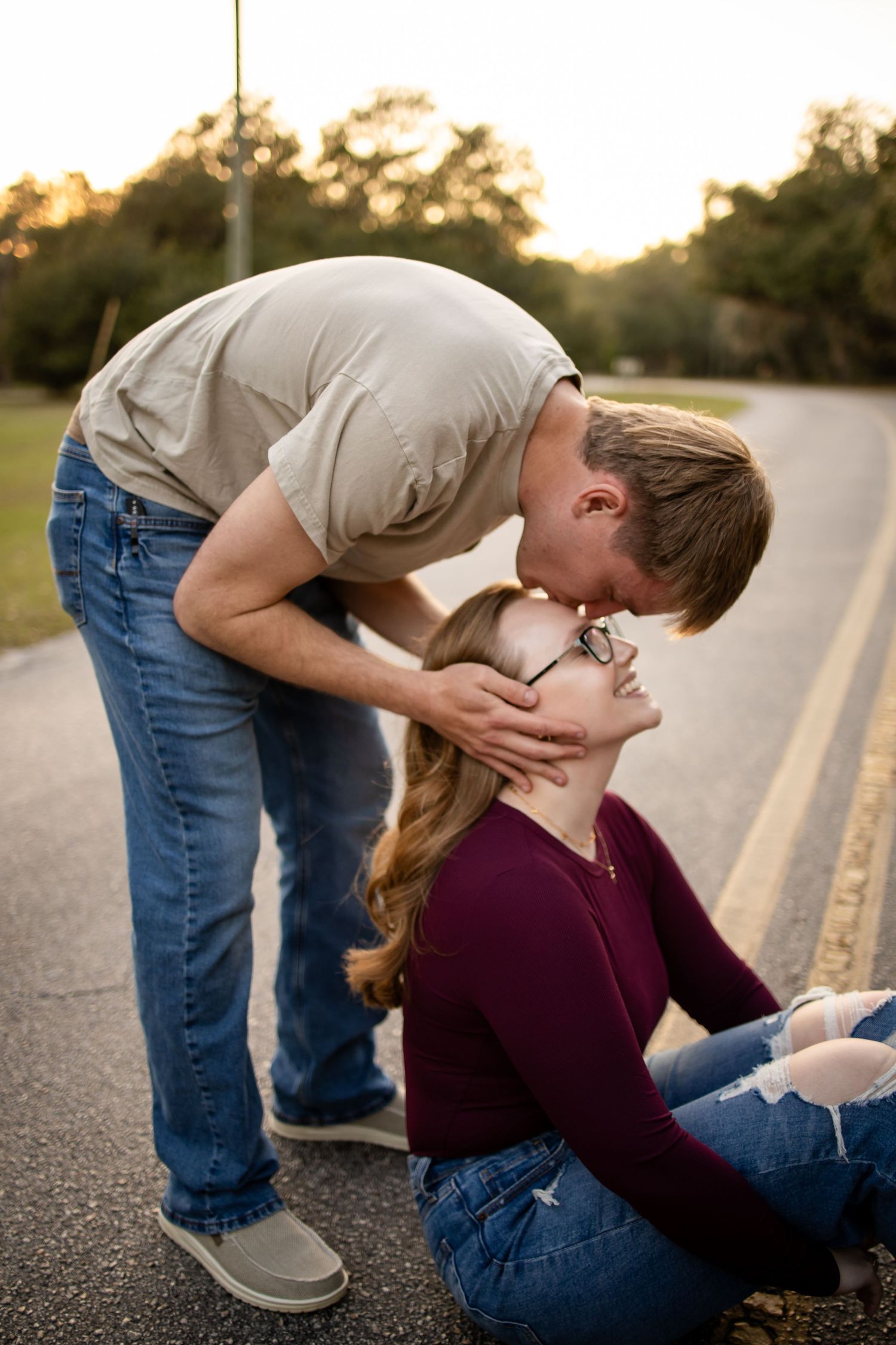 Couple shares a tender kiss on a rural road at sunset.