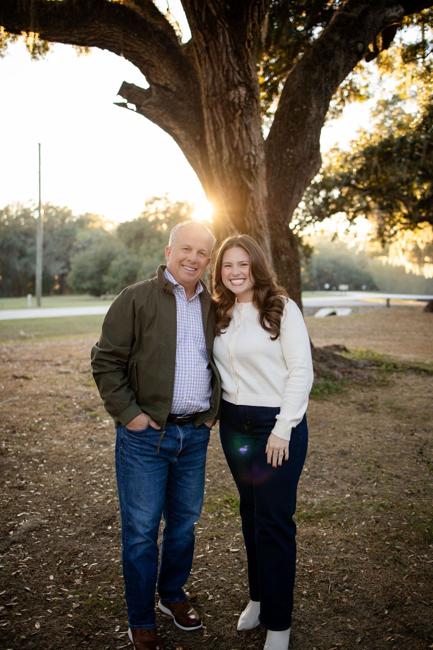 Family photo shoot under large oak trees with warm sunset lighting in the background.