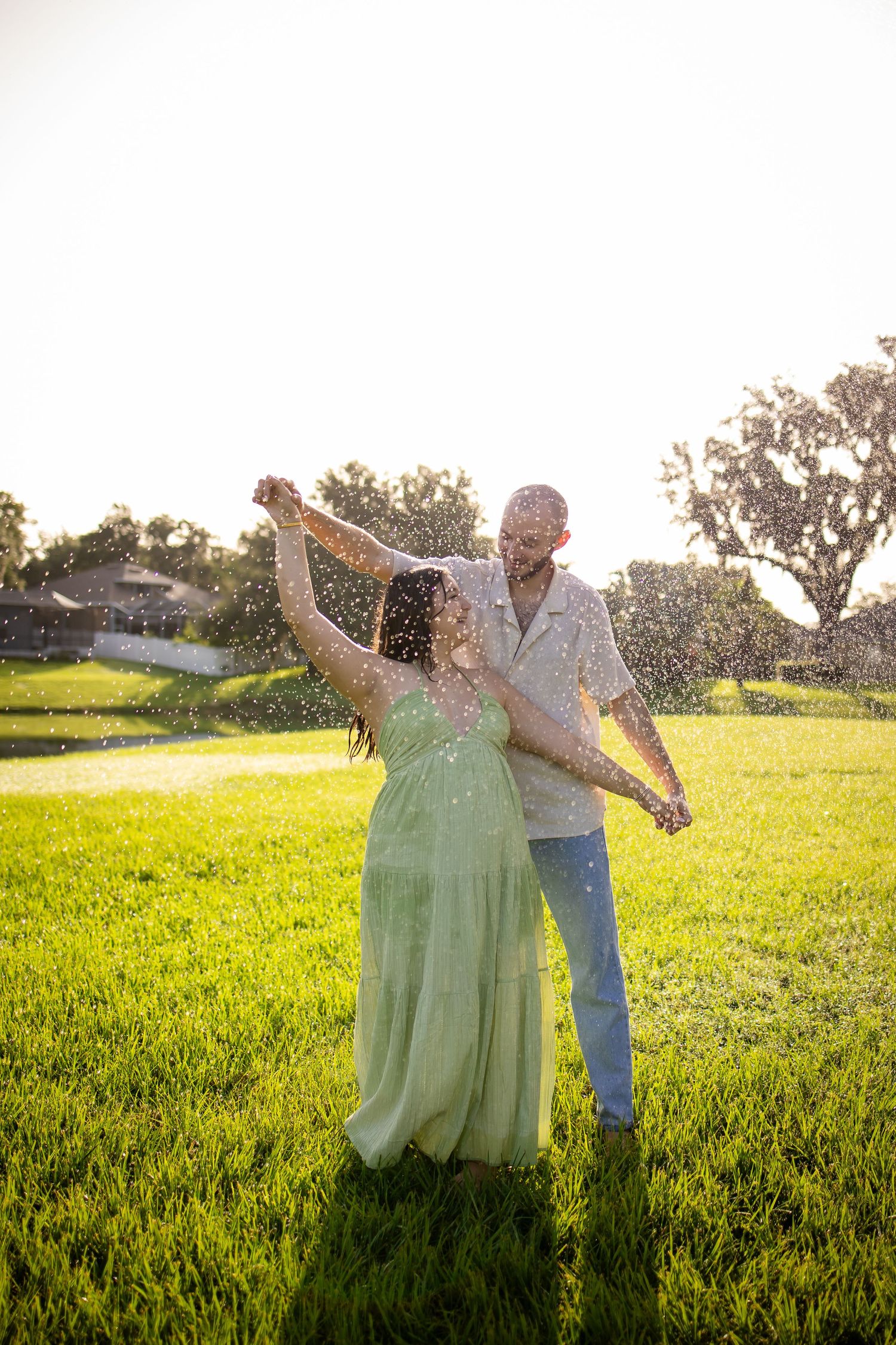A couple dances together in a sunlit meadow at sunset with water droplets sparkling around them.