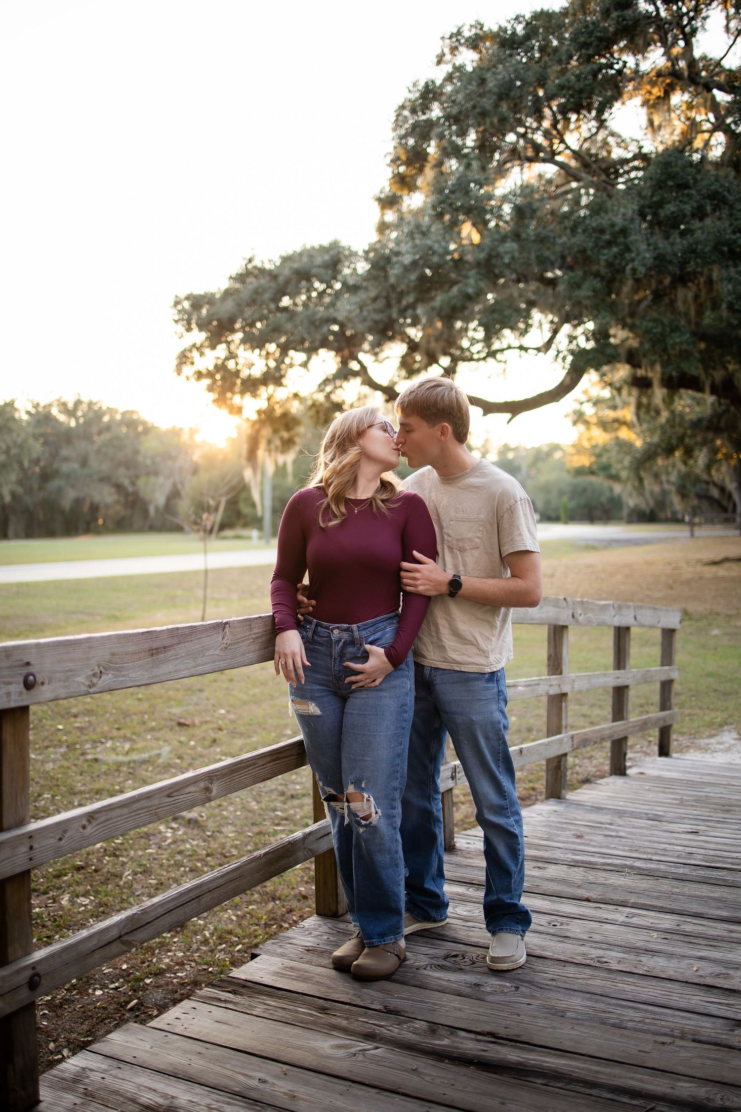 Romantic couple sitting together on a wooden bridge at sunset in a park setting.