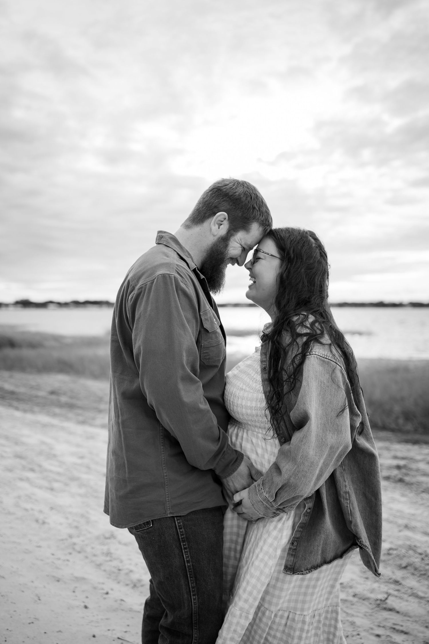 Couple shares an intimate moment on a cloudy beach while wearing casual attire.
