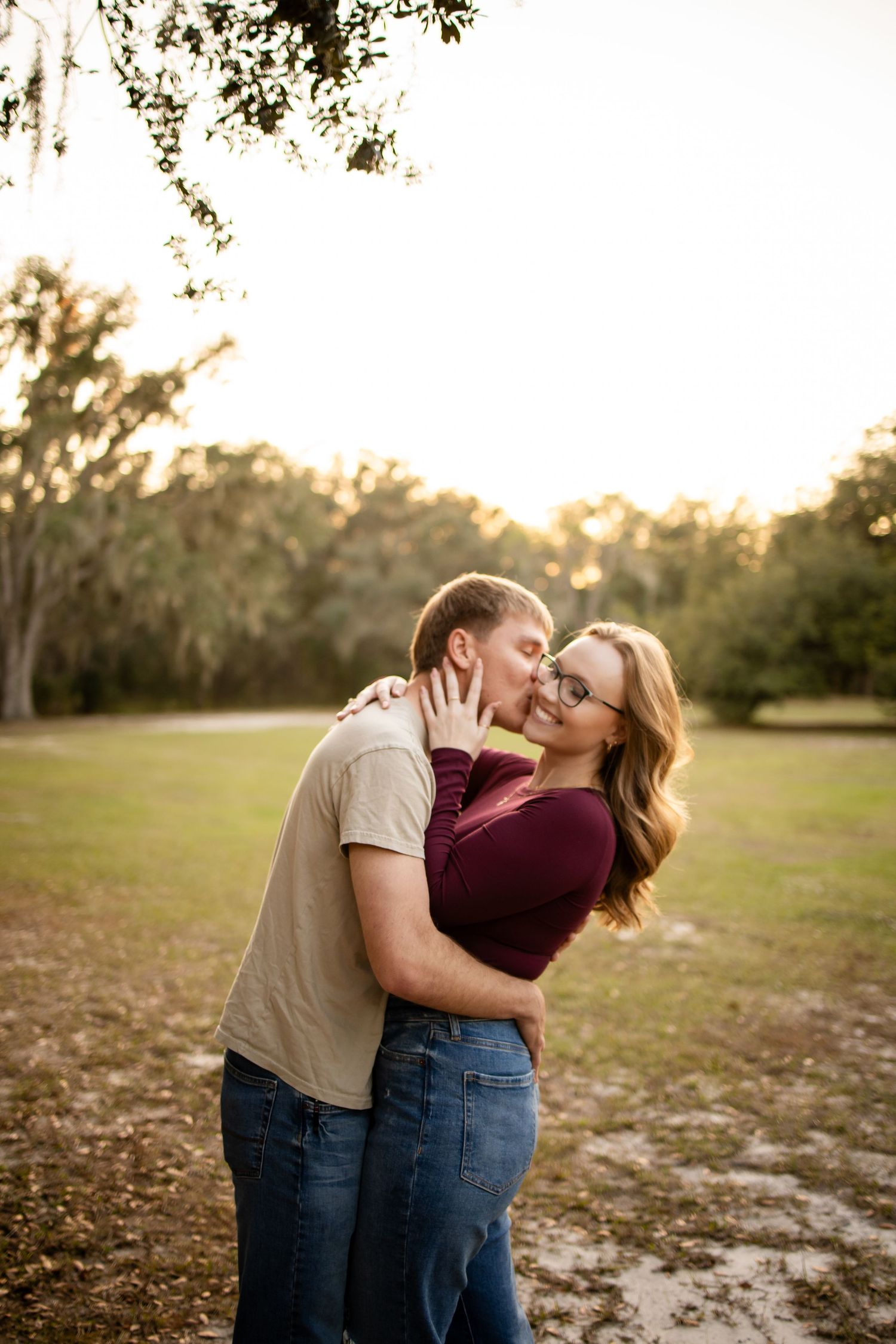 A romantic couple shares an intimate moment in a sunlit field wearing casual clothing.