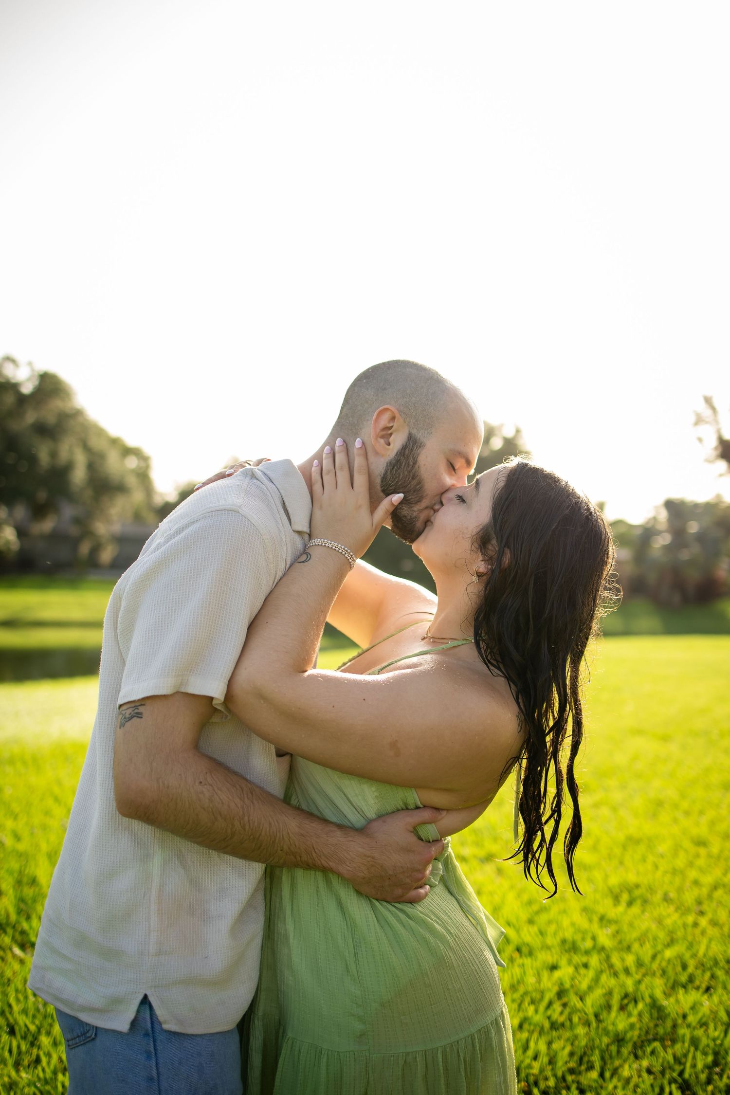 Couple embraces and shares tender moments in a sunlit green field during golden hour.