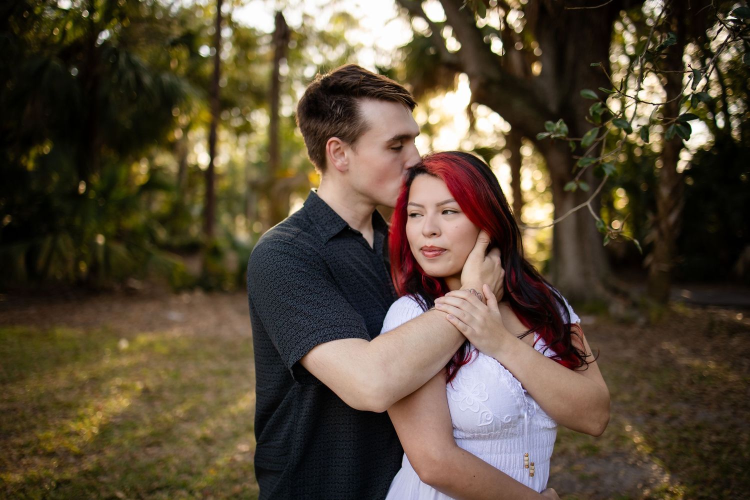 A couple embraces tenderly in a sunlit wooded area during a romantic outdoor photo session.