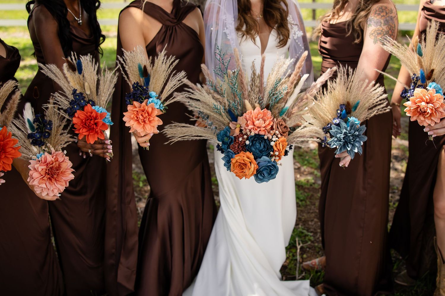 Bridesmaids in brown dresses holding boho bouquets with pampas grass, orange dahlias, and teal flowers at a wedding.