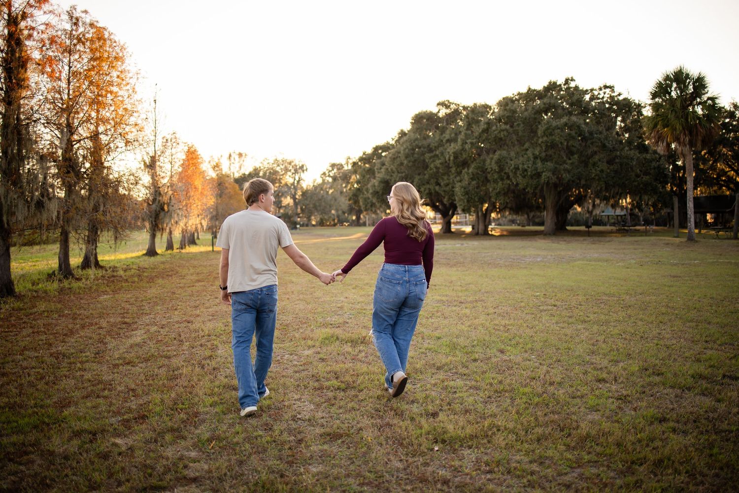 Couple walking together in a park at sunset with autumn trees in the background.