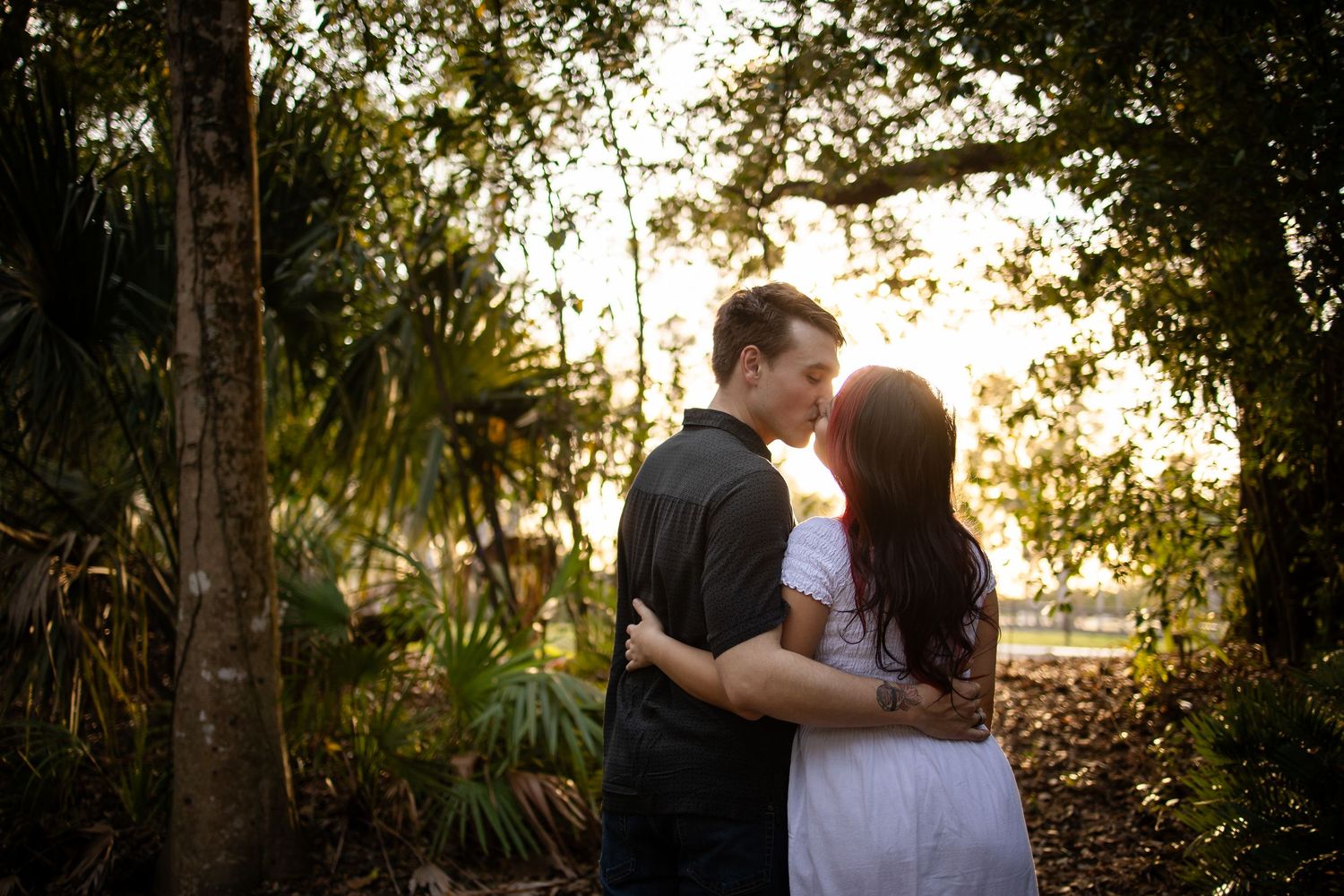 A romantic couple shares a tender moment in a sunlit garden setting during a golden hour engagement photo session.