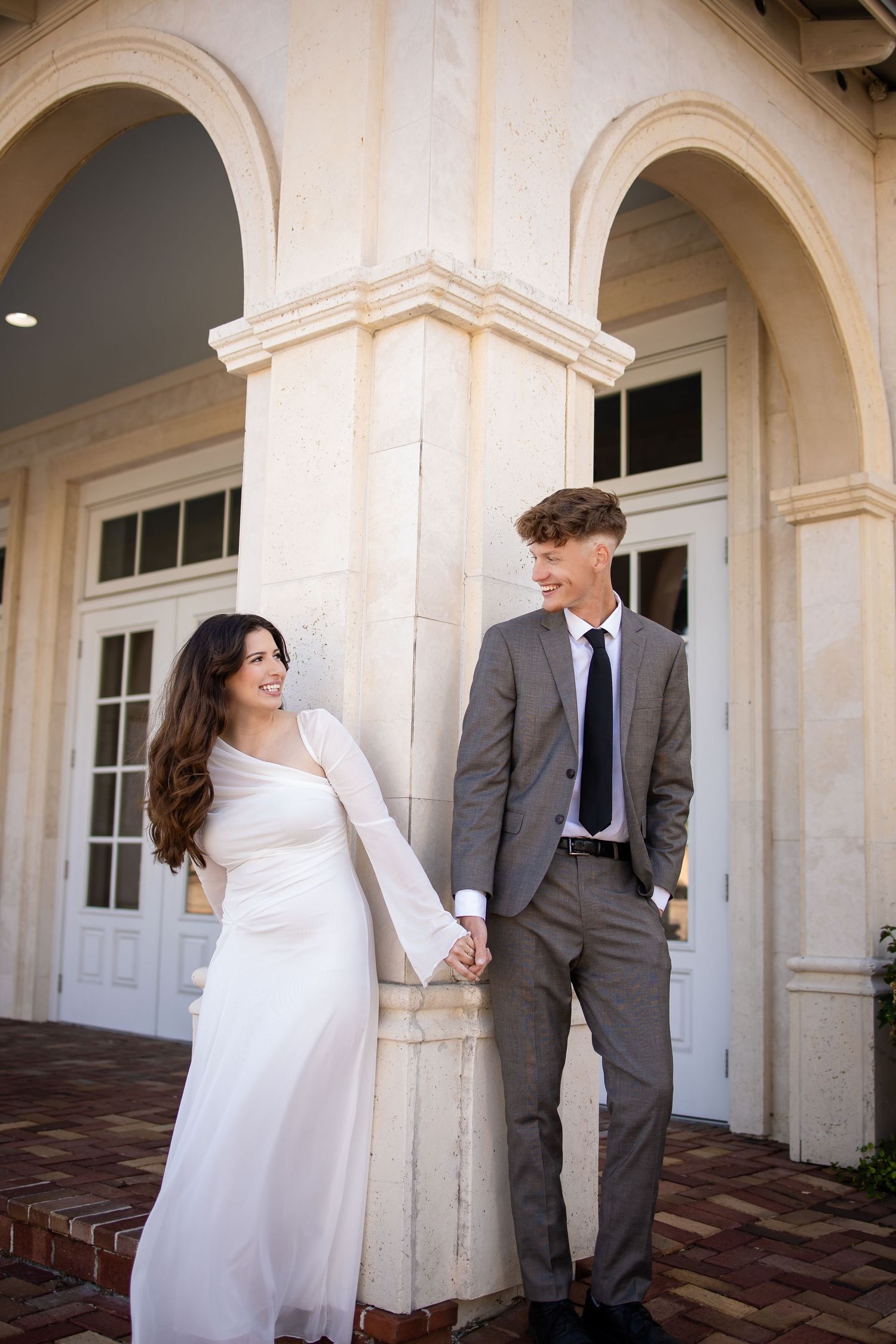 Couple in wedding attire poses against elegant white archways and columns.