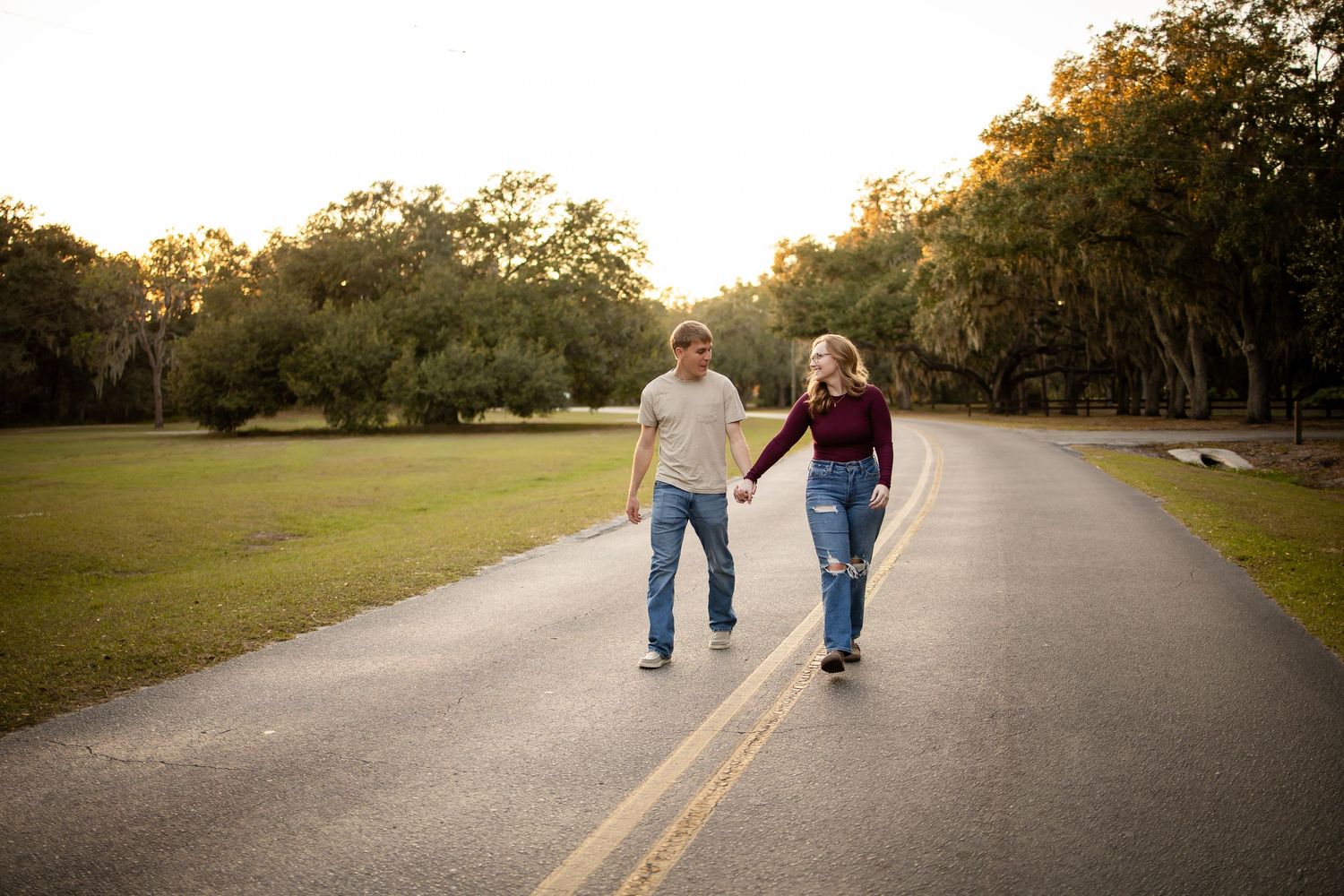 Couple strolling hand in hand down a tree-lined road at sunset.