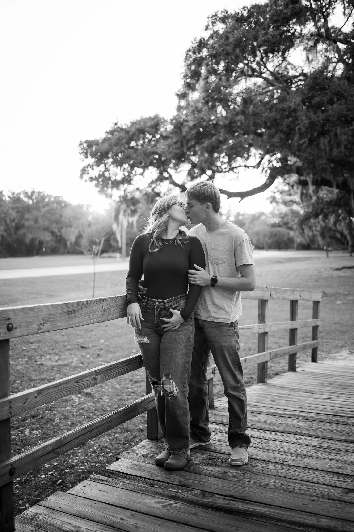 Black and white photo of a couple sharing an intimate moment on a wooden boardwalk.