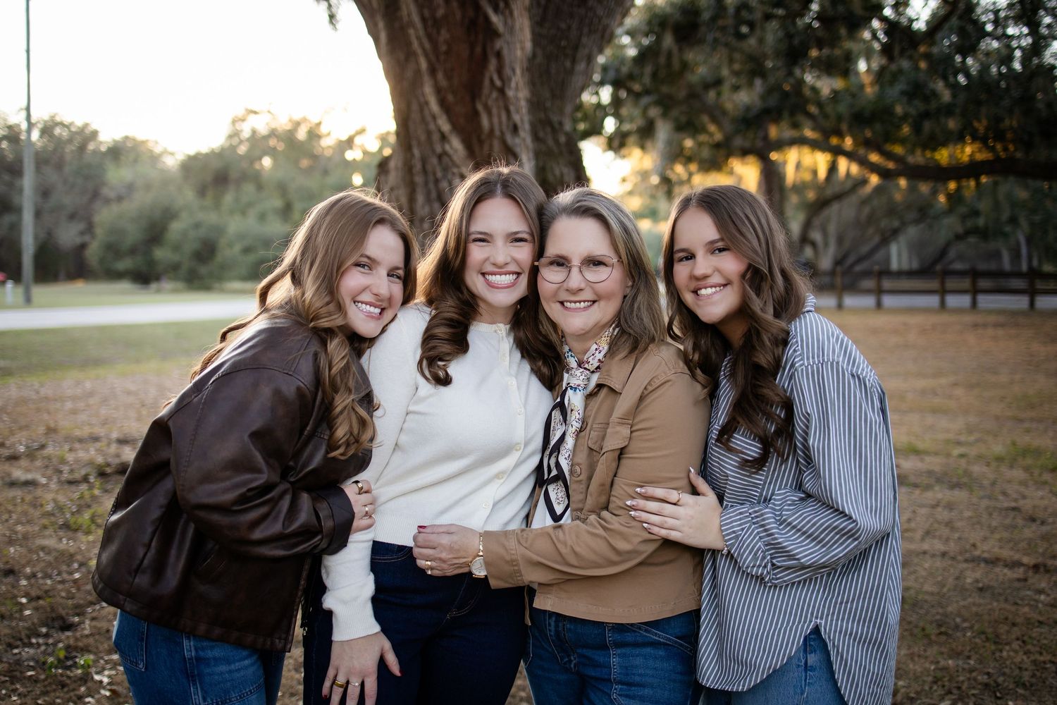 Group of people in coordinated outfits embrace while laughing under large tree.