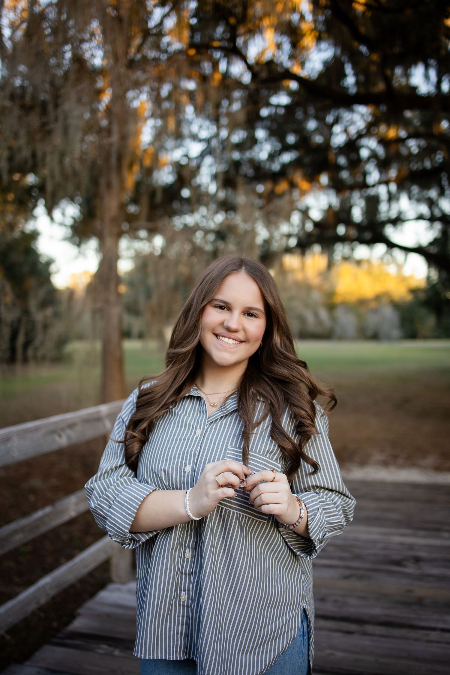 A person in a striped shirt stands on a wooden bridge surrounded by Spanish moss trees.