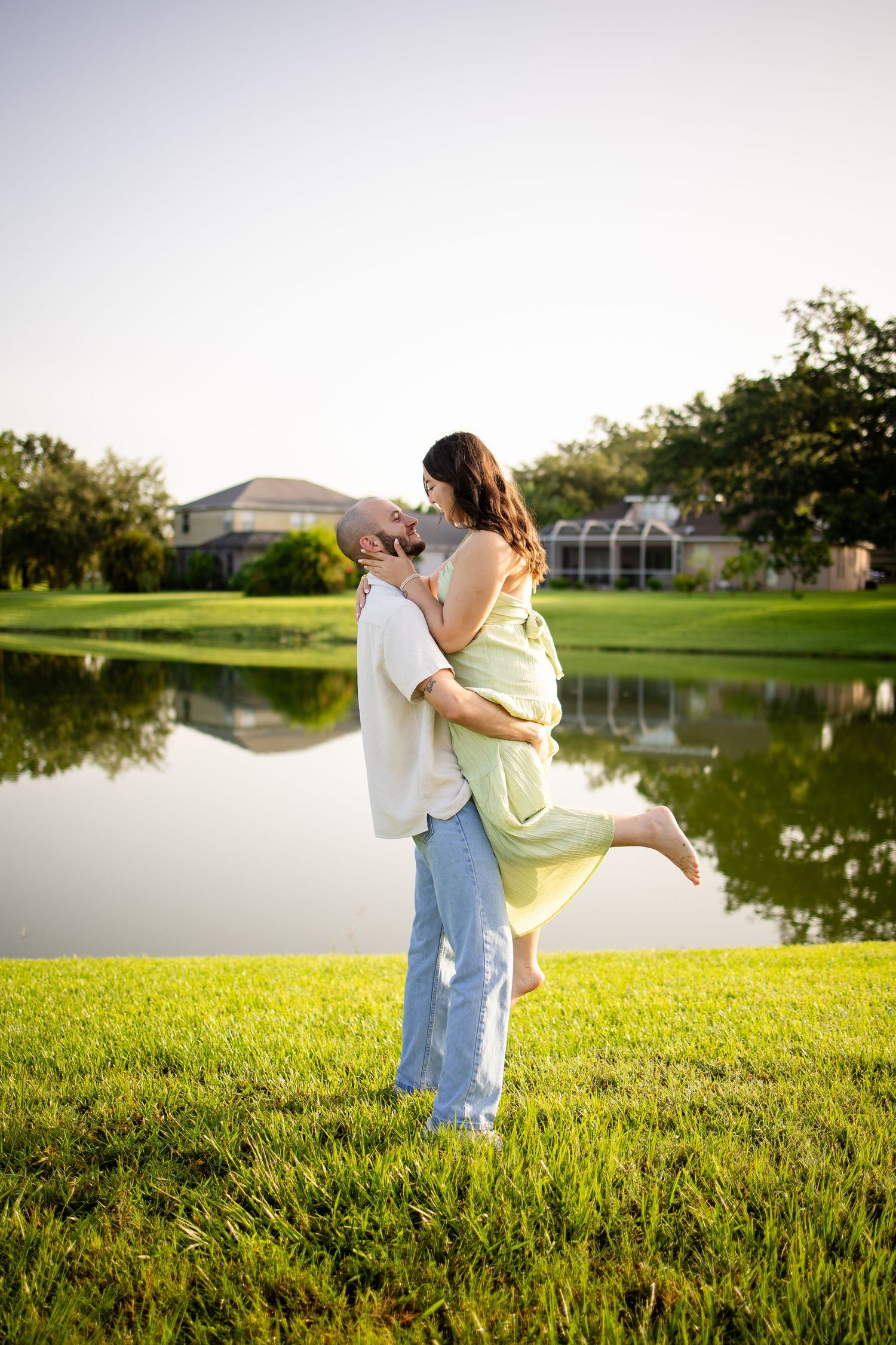 A romantic couple embraces by a scenic lake at sunset, with the woman in a light green dress lifted up.