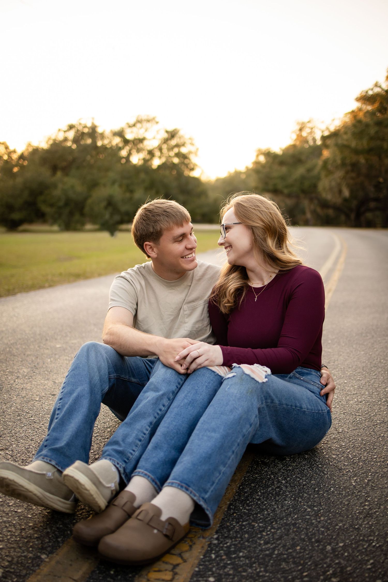 A couple sits together on a road during golden hour sharing a loving moment.