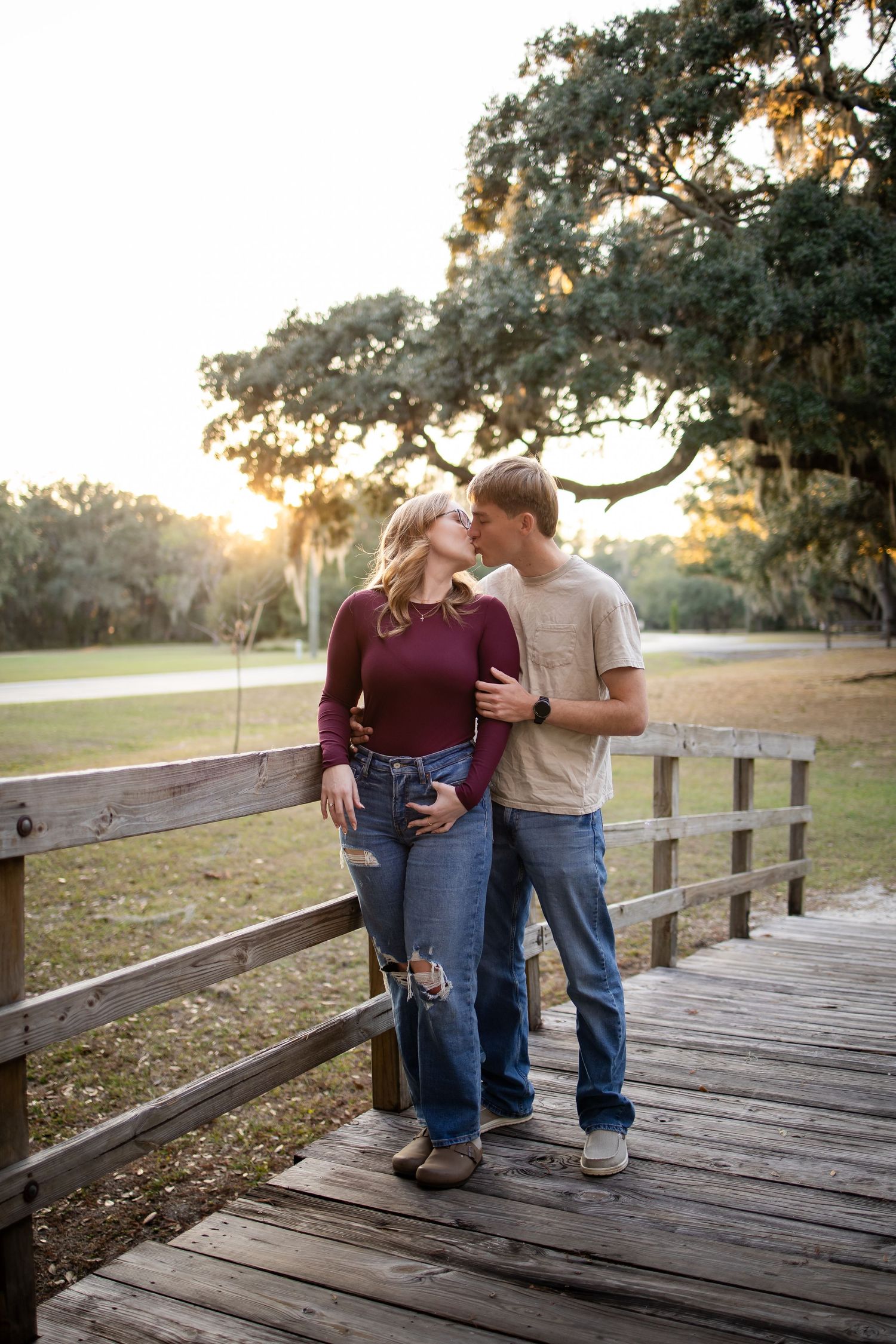 A romantic couple shares an intimate moment on a wooden boardwalk at sunset.