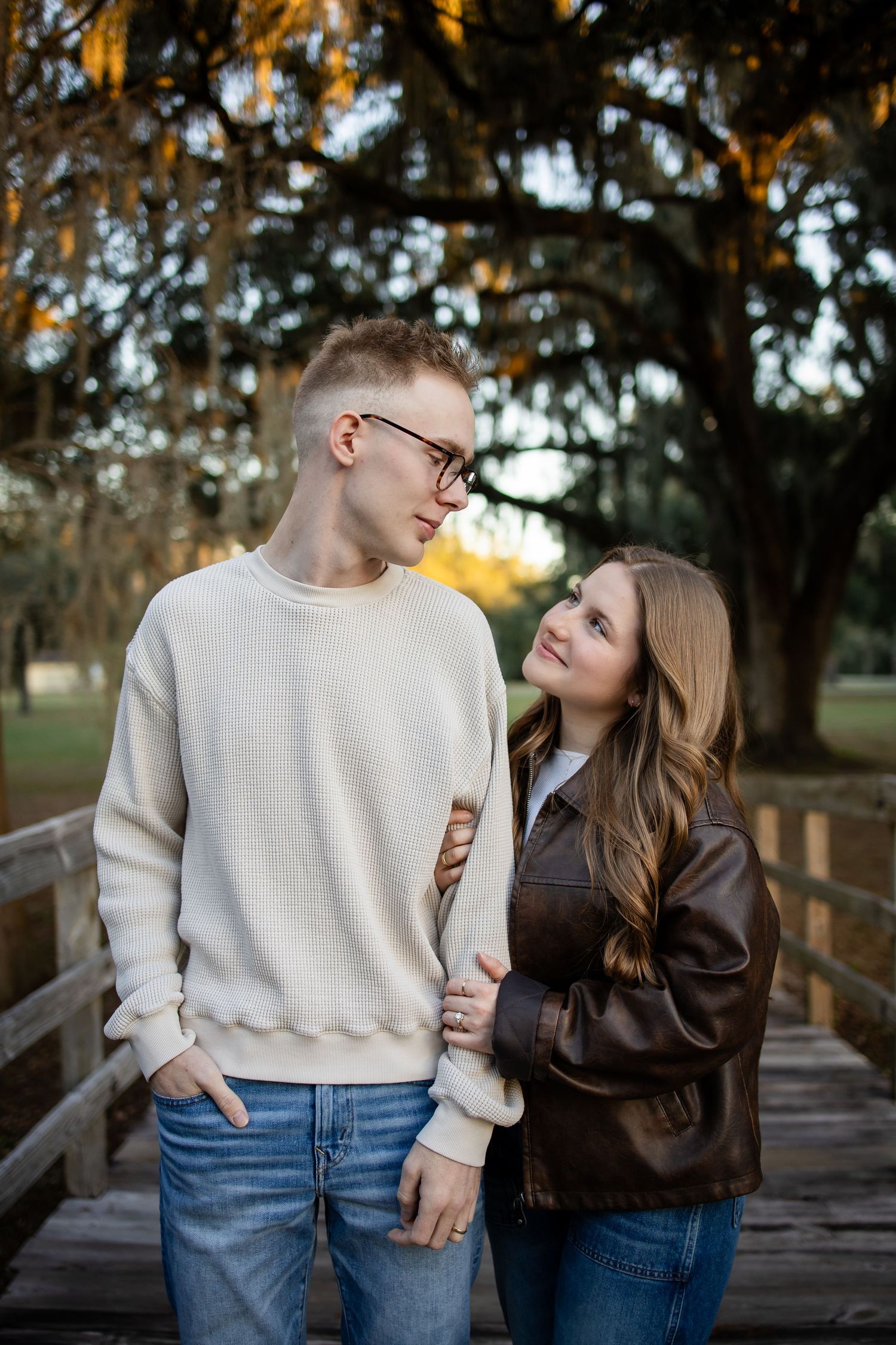 A romantic couple shares tender moments on a wooden bridge during golden hour in a park setting.