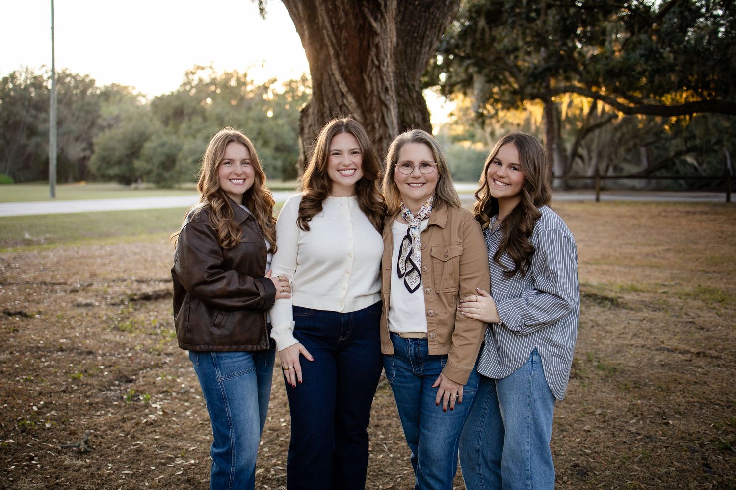 A group of people in casual clothing standing together outdoors under large oak trees.