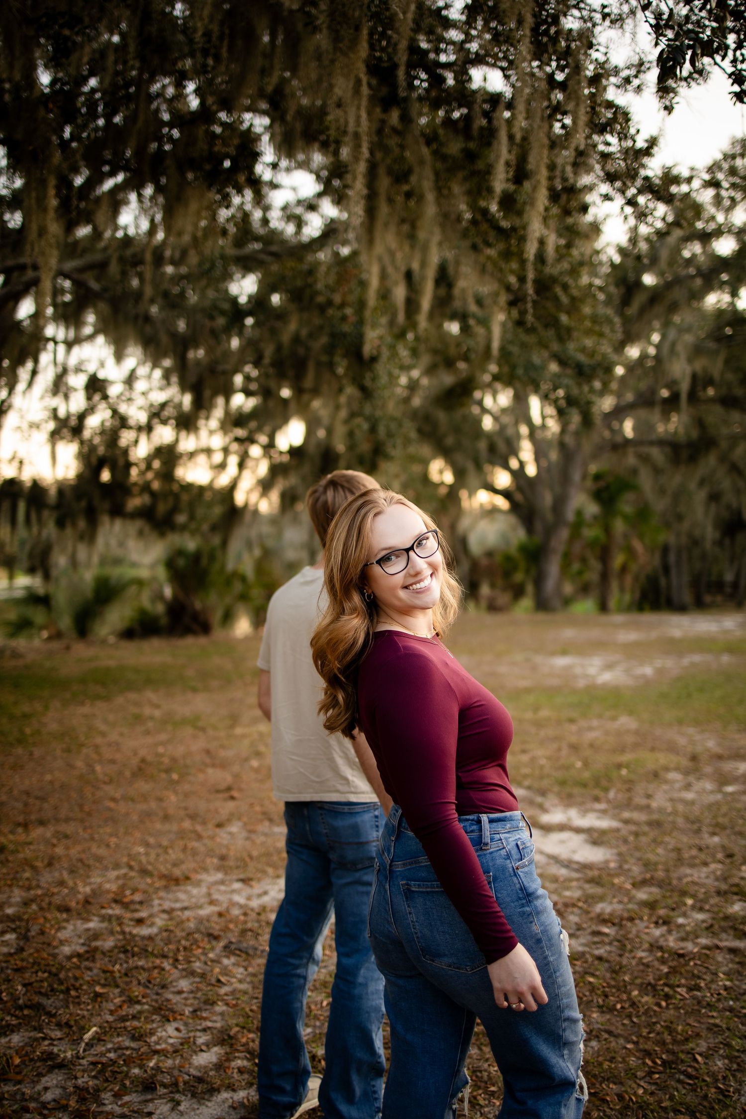 A couple shares a joyful embrace in a park with Spanish moss hanging from trees.
