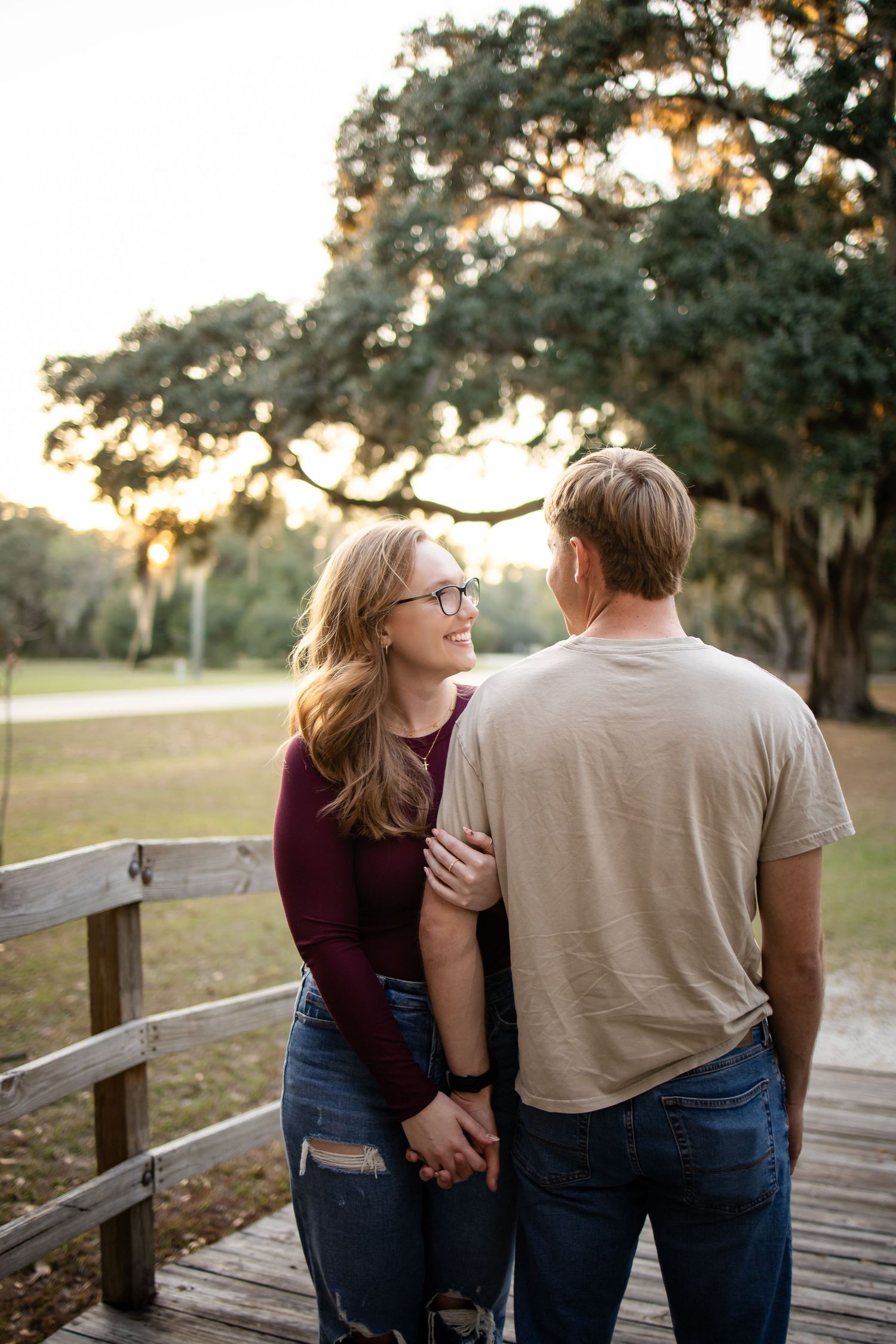 Intimate moment between couple on wooden bridge with Spanish moss trees in background.