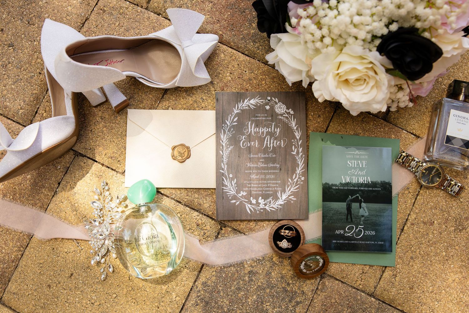 Elegant wedding flat lay featuring white heels, floral bouquet, wood invitation, wax seal envelope, perfume, and gold ring box.