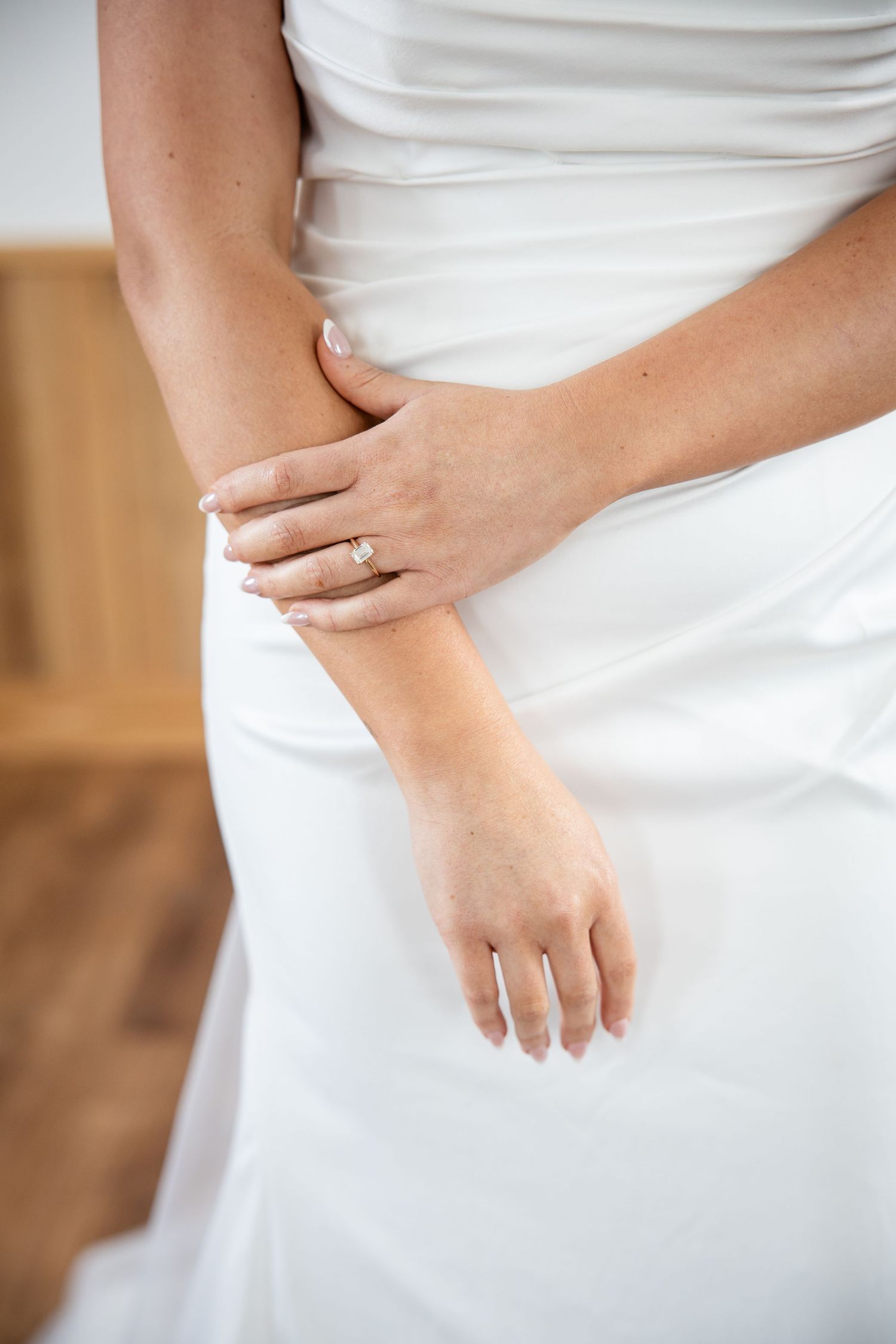 Close-up of a bride in a white wedding dress showing her diamond engagement ring on her finger.