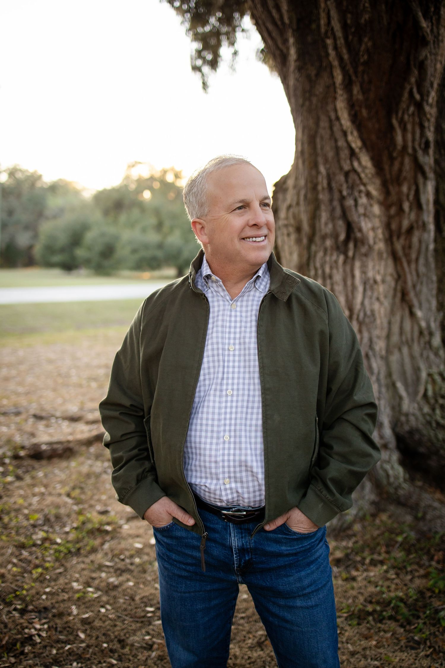 Casual outdoor portraits of someone in a checkered shirt and olive jacket leaning against a large tree.