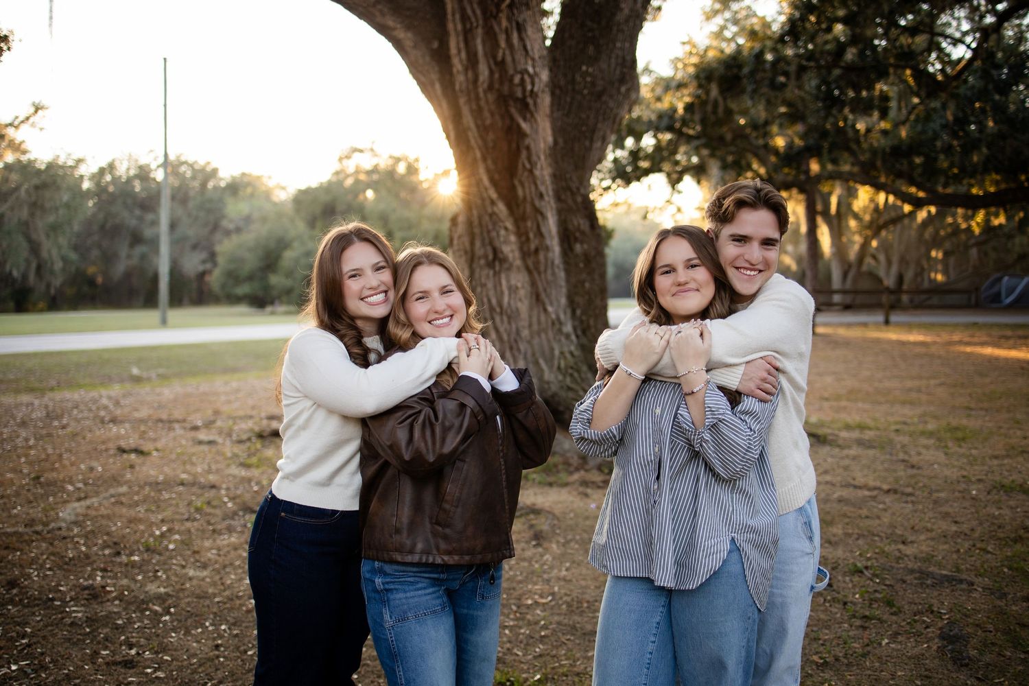 Candid group photo showing people embracing and laughing under large tree.