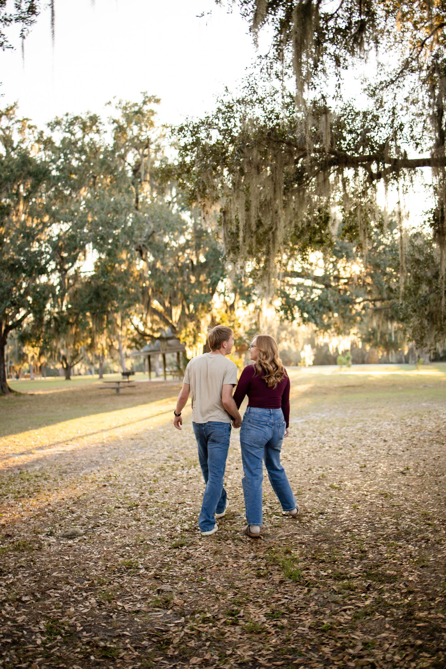 A couple walks together on a path under Spanish moss-draped trees during golden hour.
