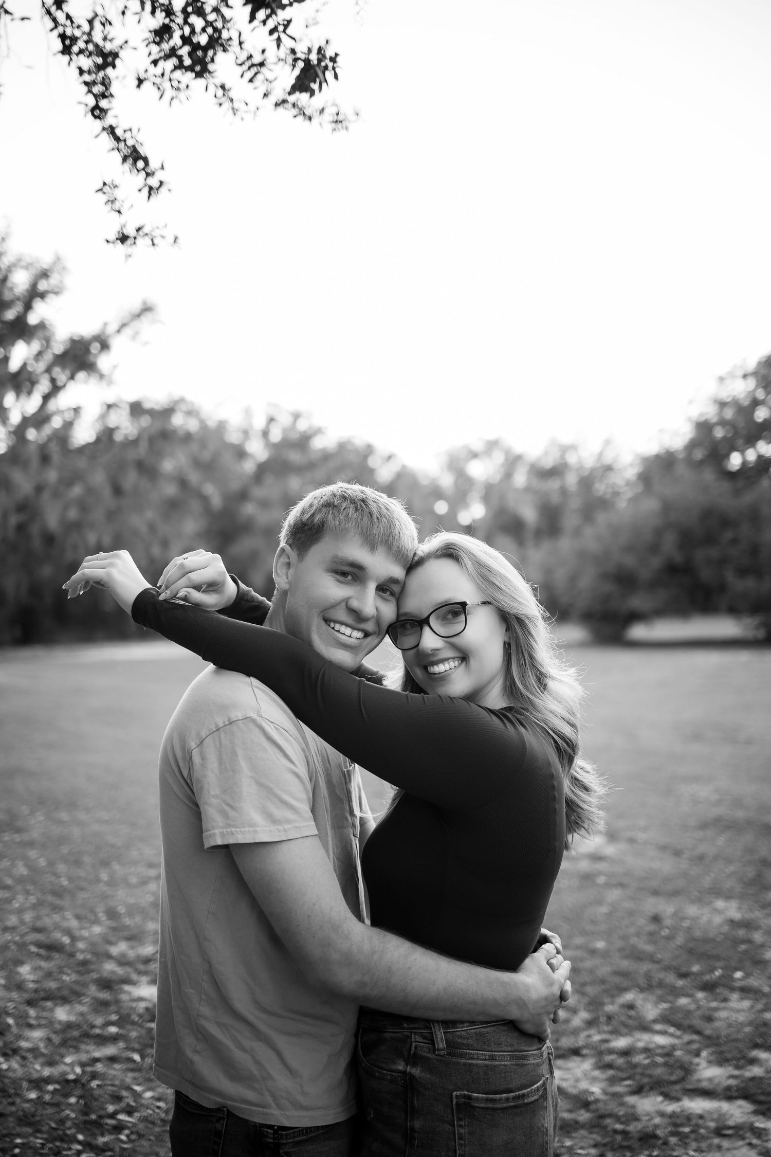 A black and white portrait of a couple laughing and embracing in an open field.