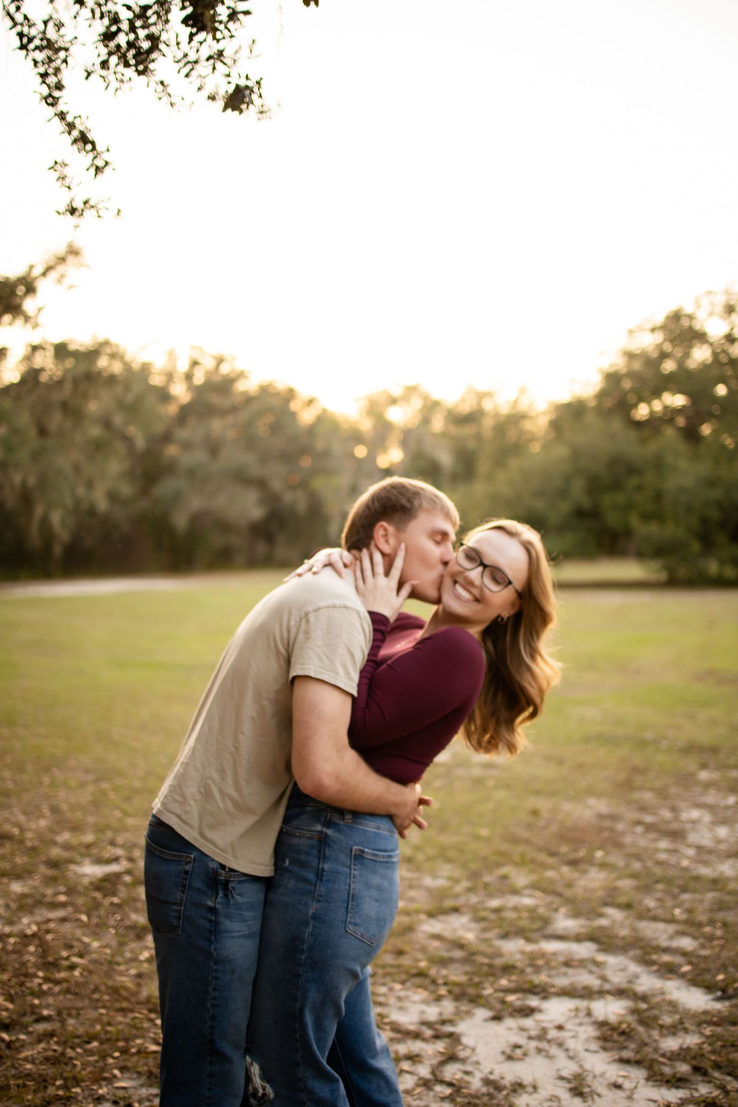 Playful couple laughing and embracing in a park during golden hour.