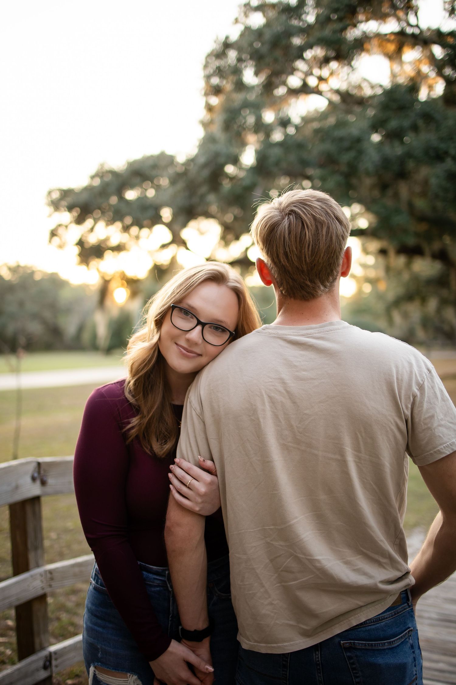 A couple shares a tender moment while leaning on a wooden fence during golden hour.