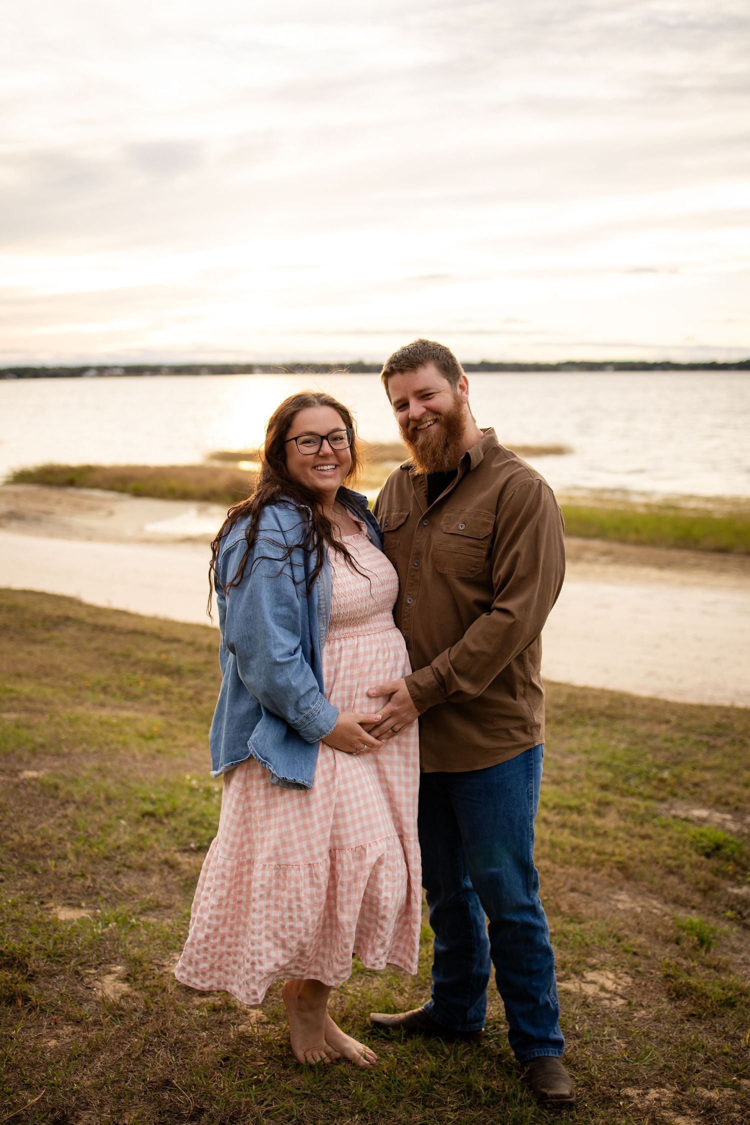 Couple shares tender moment during beach maternity photoshoot at dusk.