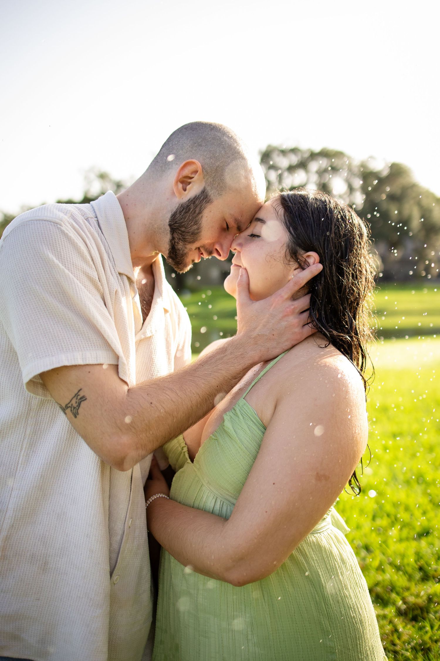 A romantic couple shares a passionate kiss in a sunlit field while wearing light colored attire.