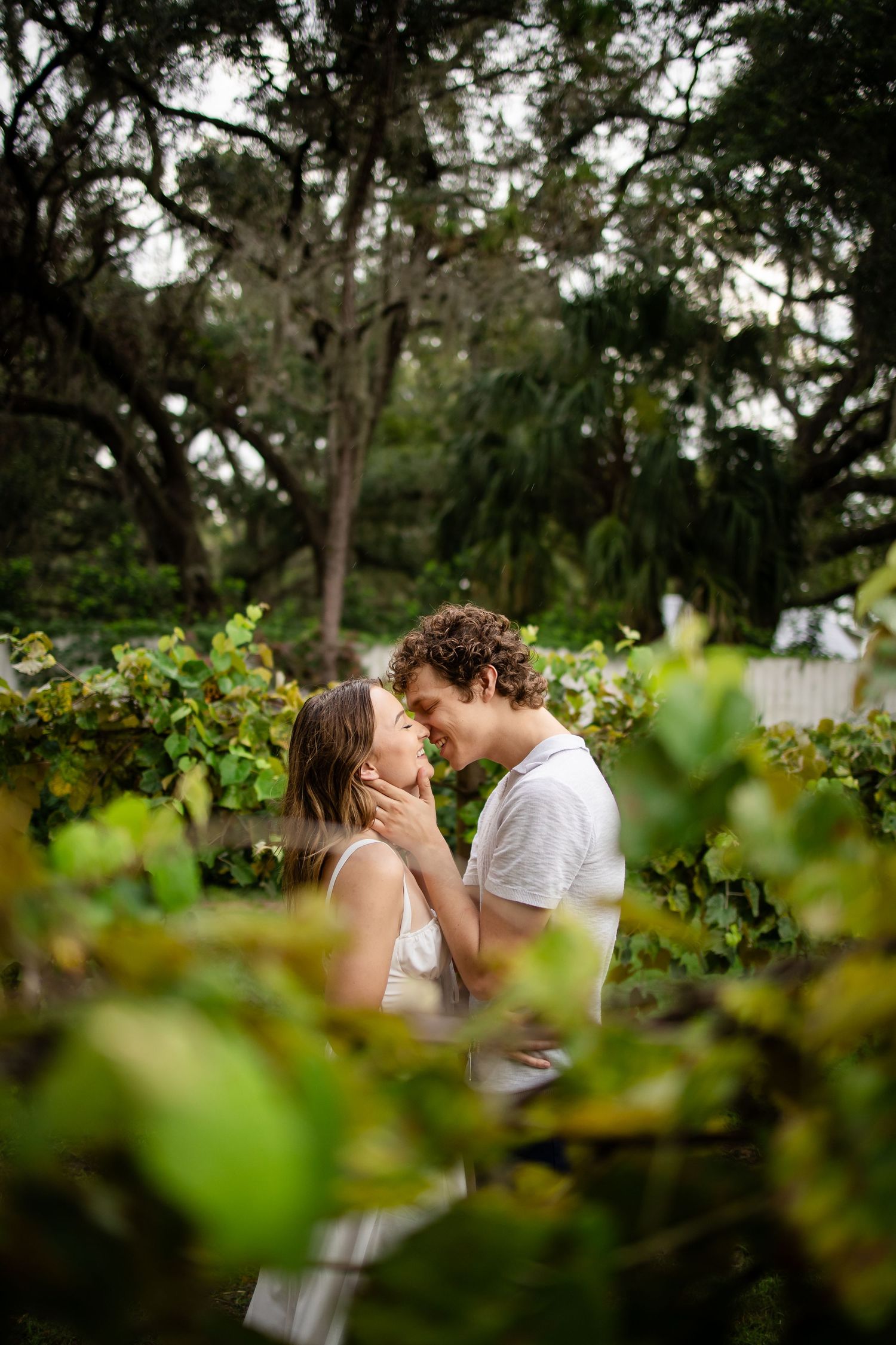 A couple shares an intimate moment together among lush green foliage in a garden setting.