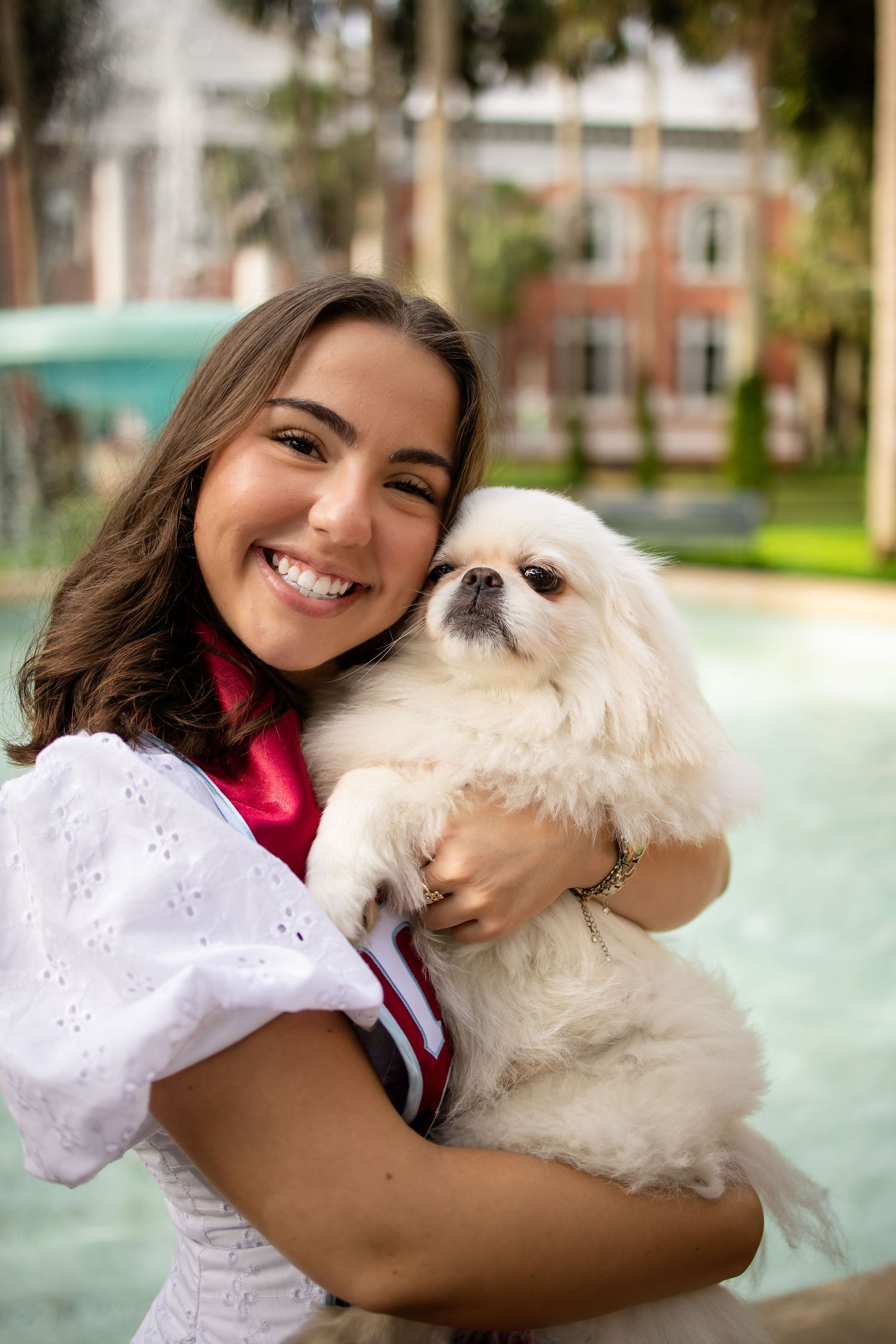 A fluffy white Maltese dog shares joyful moments with someone in a pink shirt outdoors on a sunny day.