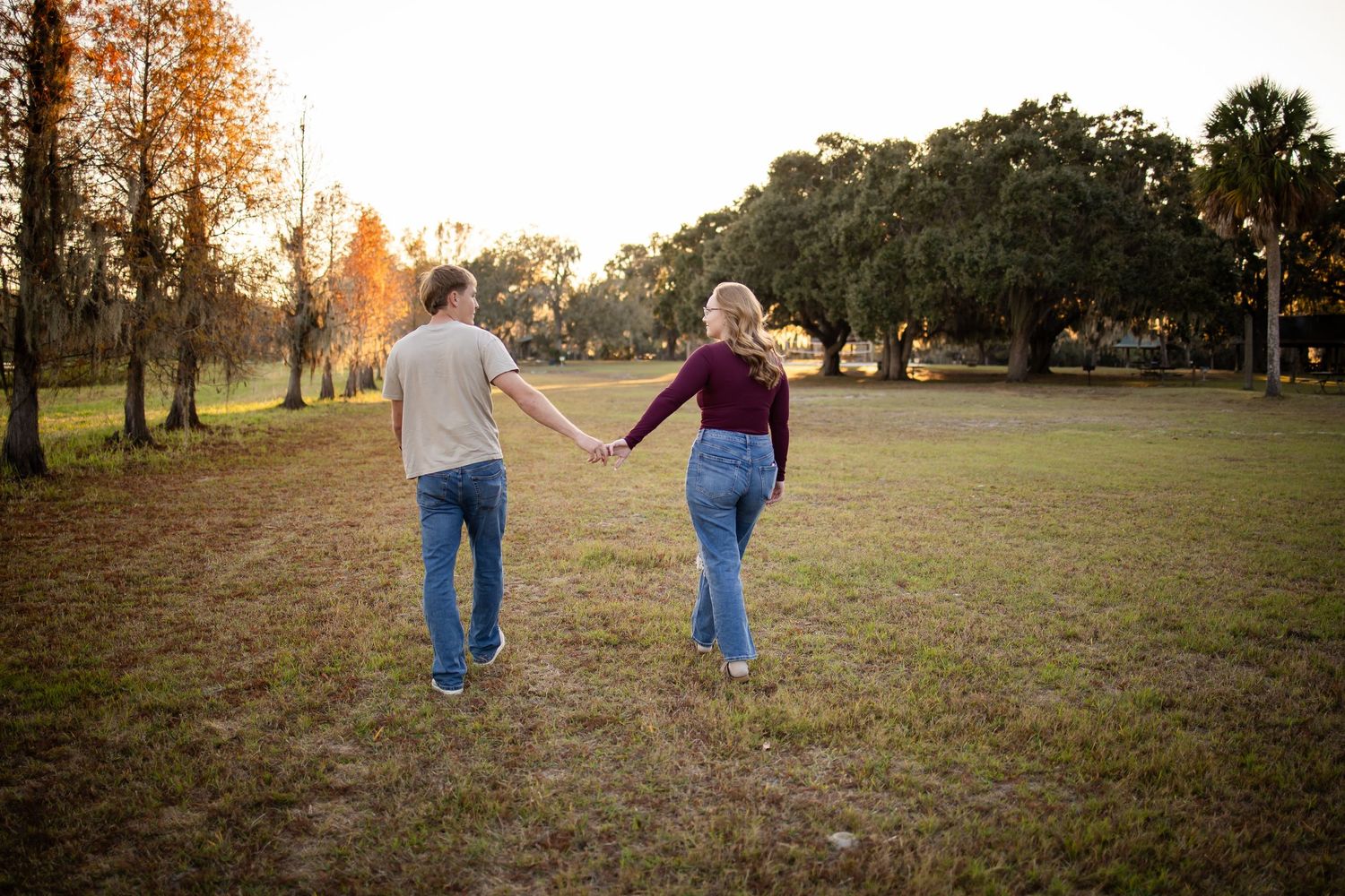 Couple walking hand in hand through a grassy field at sunset.